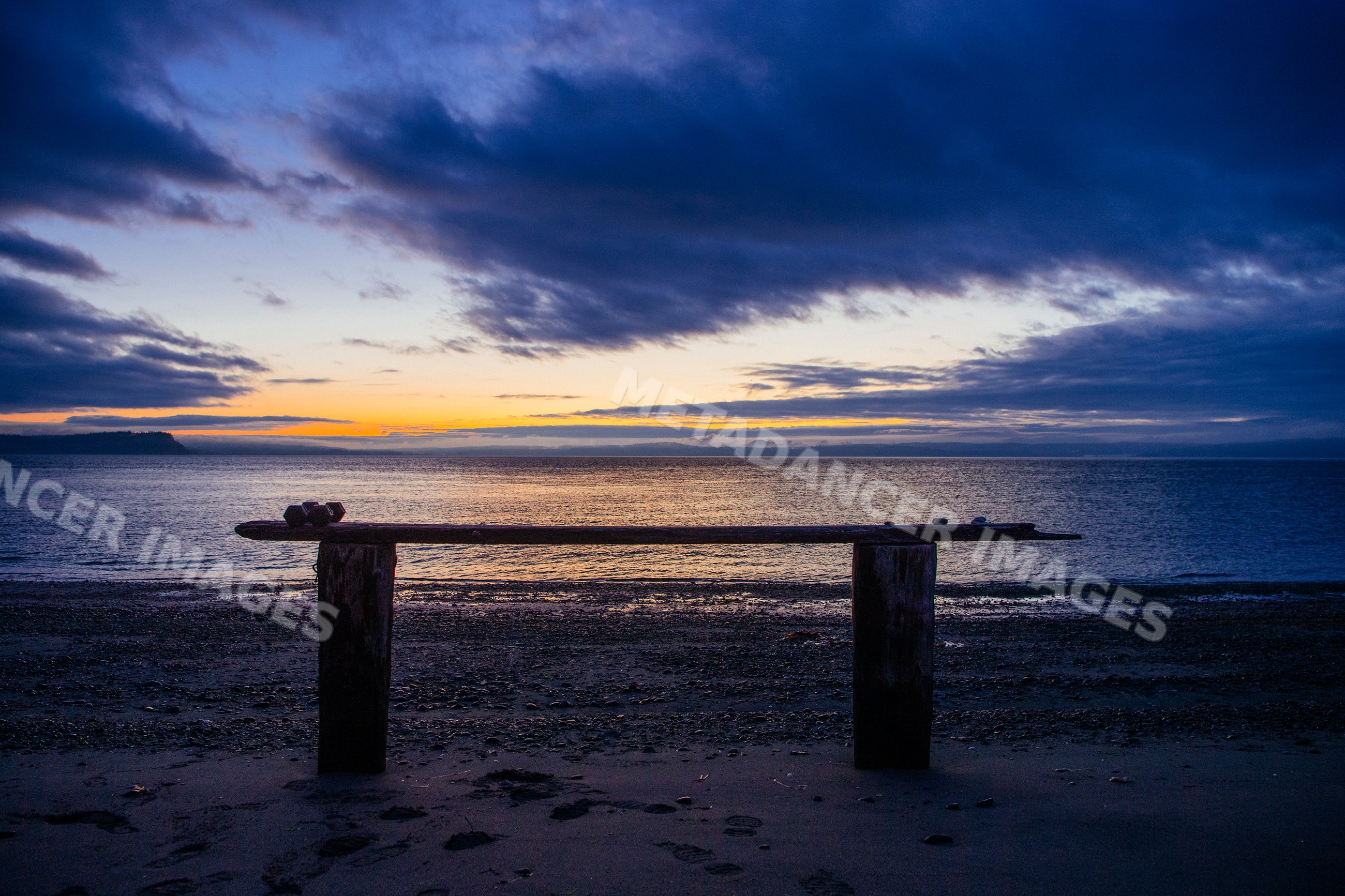 Bench silhouetted on beach at sunset over ocean in WA, USA