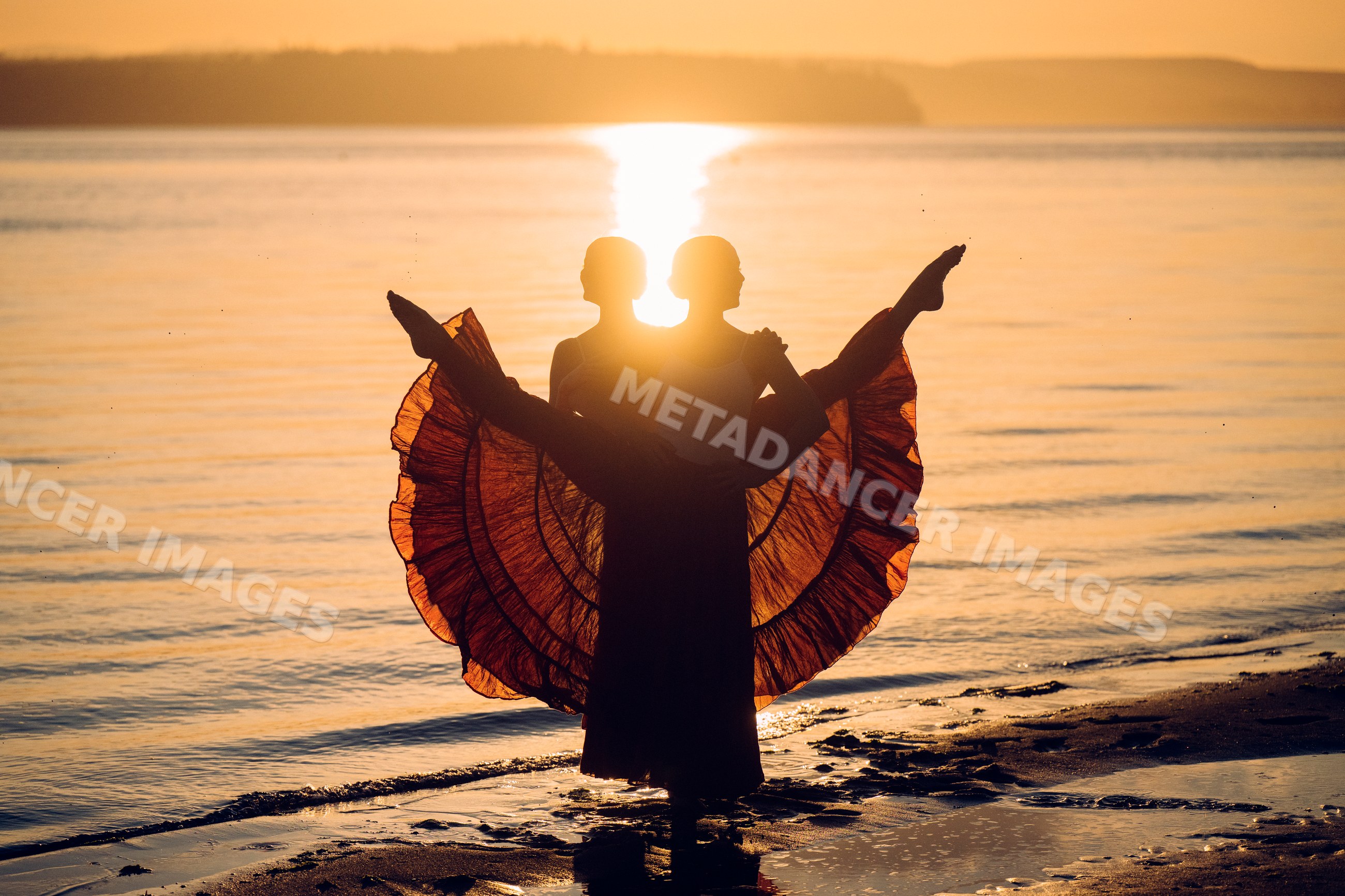 Two white women performing partner acrobatics on a beach at sunset