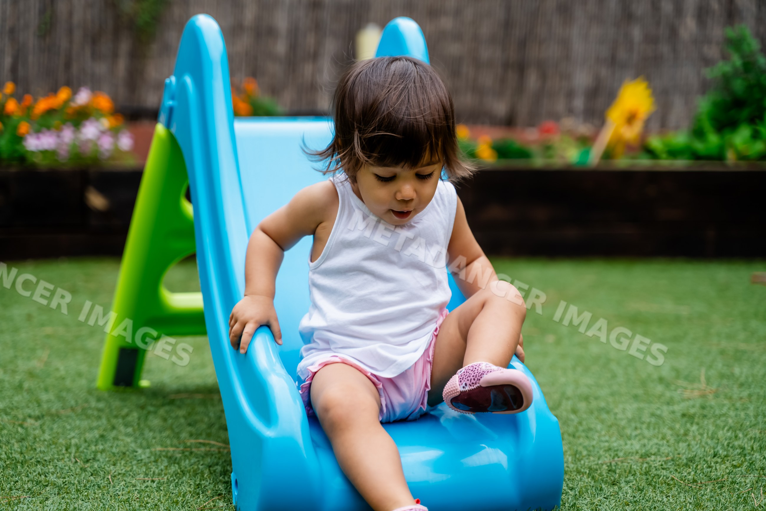 Toddler white child sliding down blue playground slide outdoors