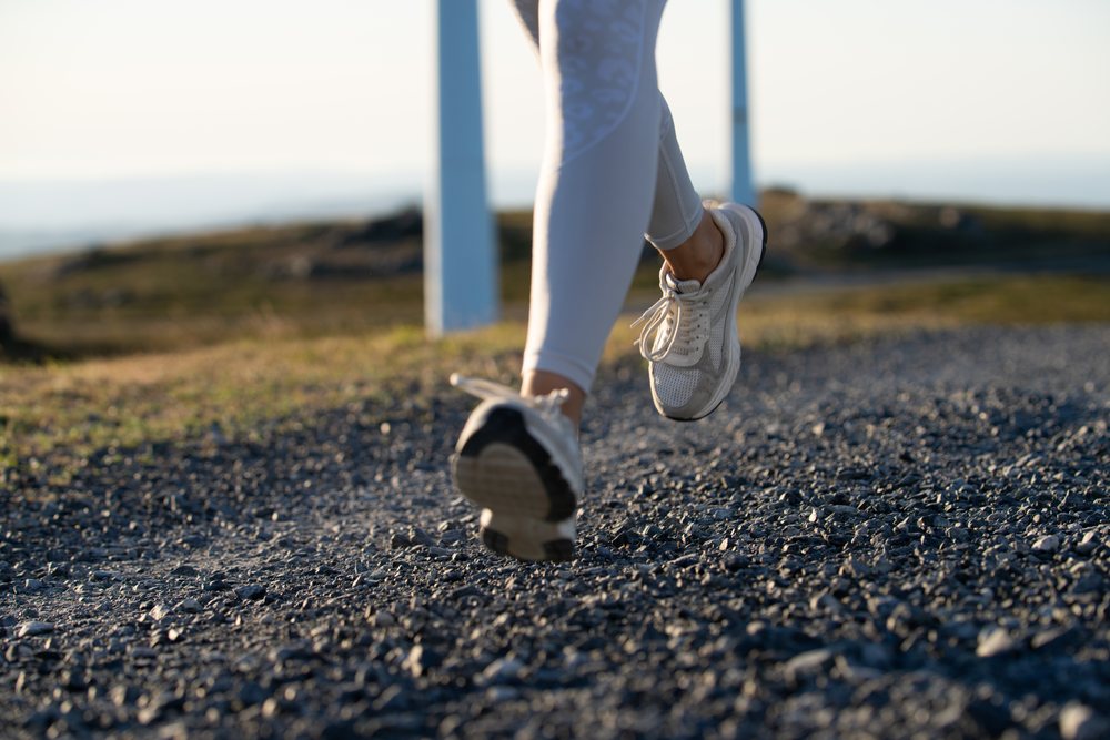 A white woman running on a gravel trail near wind turbines in Galicia