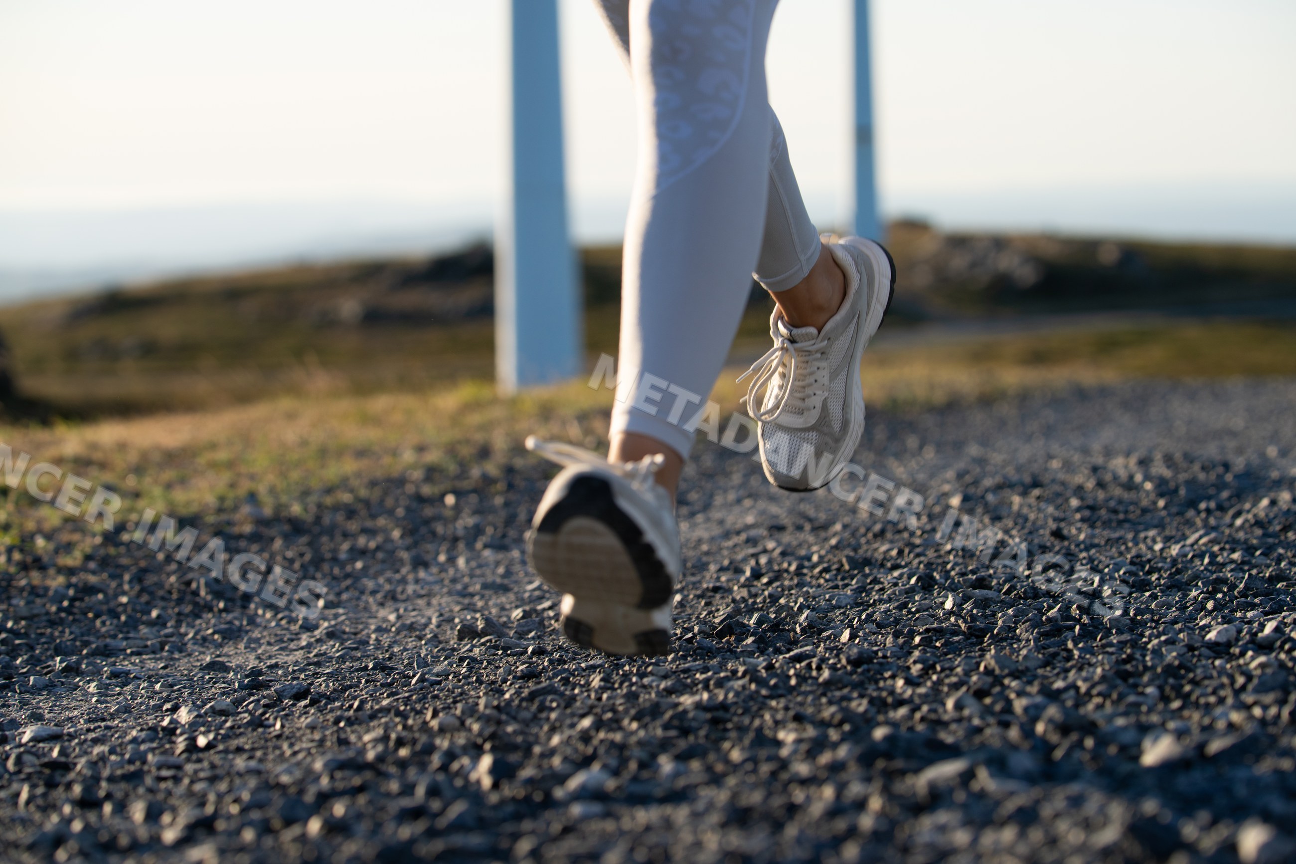 A white woman running on a gravel trail near wind turbines in Galicia