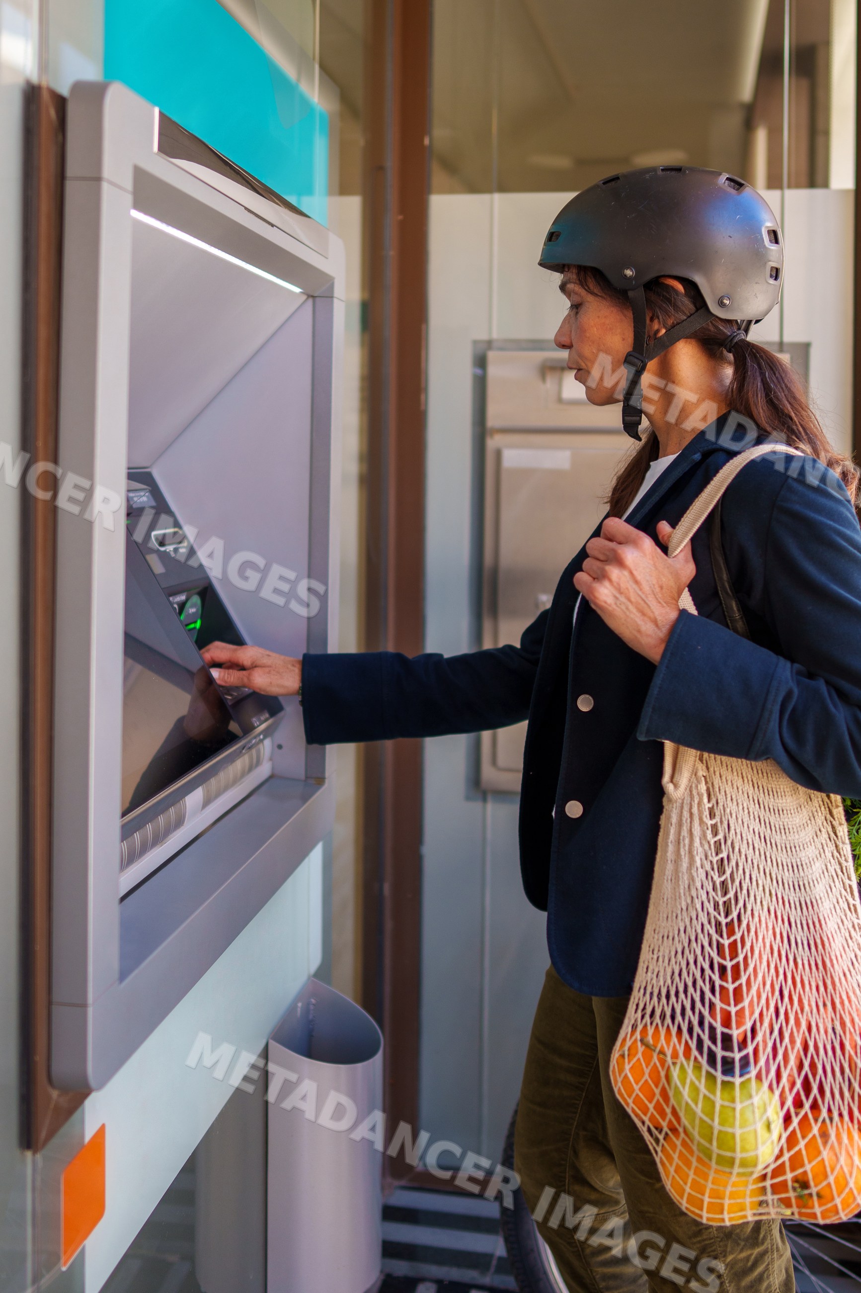 Hispanic woman using atm outdoors with shopping bag