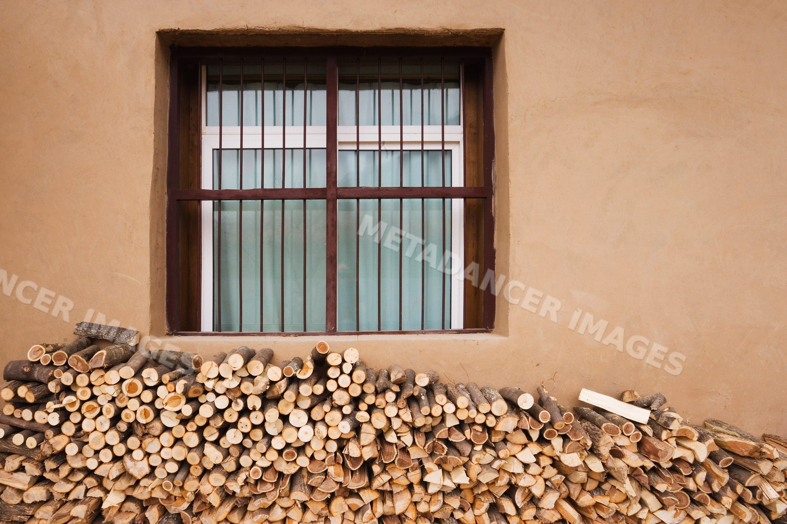 Stack of firewood logs under barred window on brown wall china