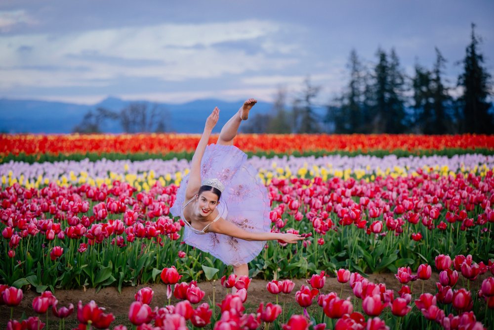 Ballet white dancer performing elegant pose in colorful tulip field