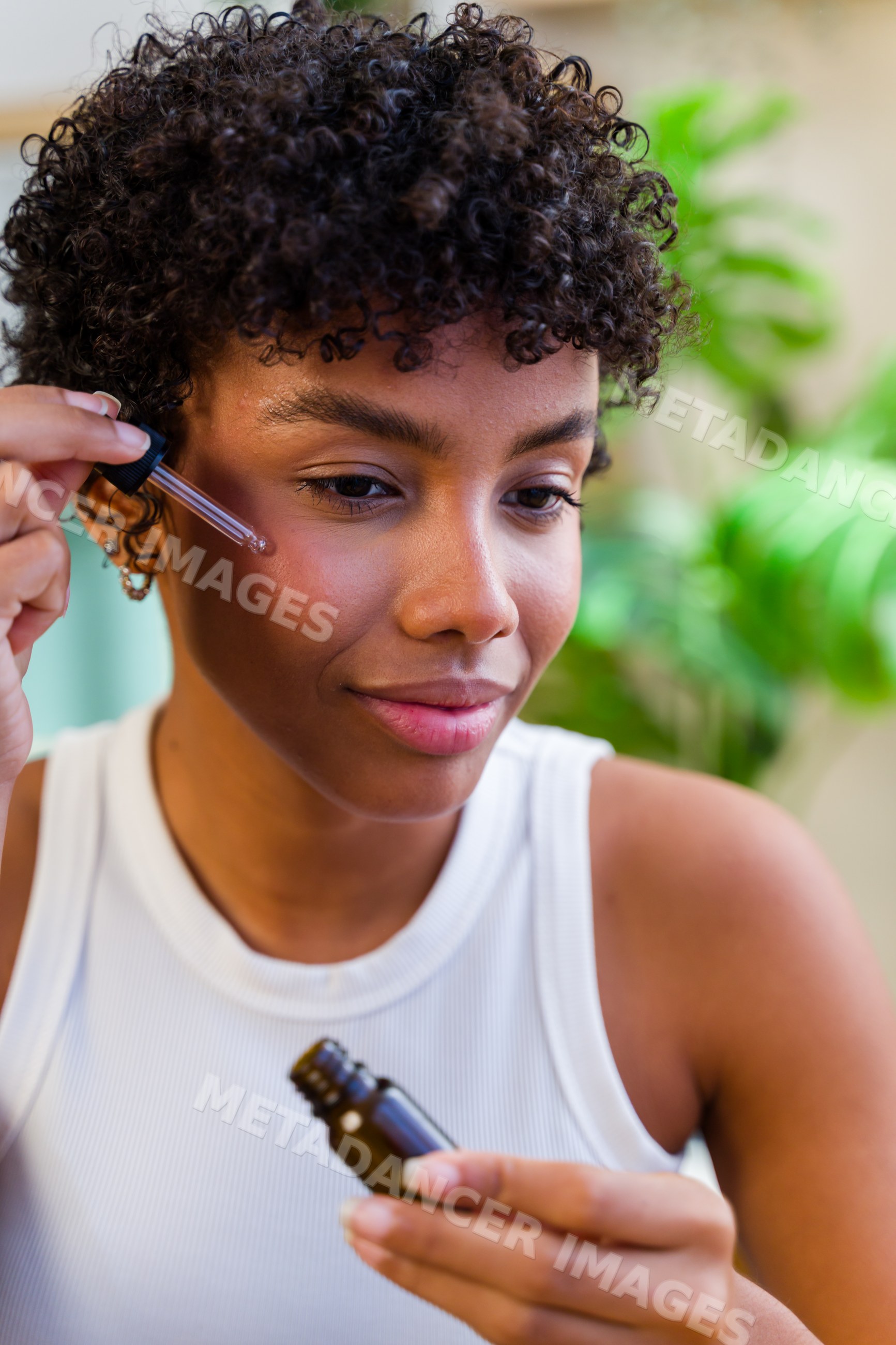 African American woman applying face serum indoors during skincare
