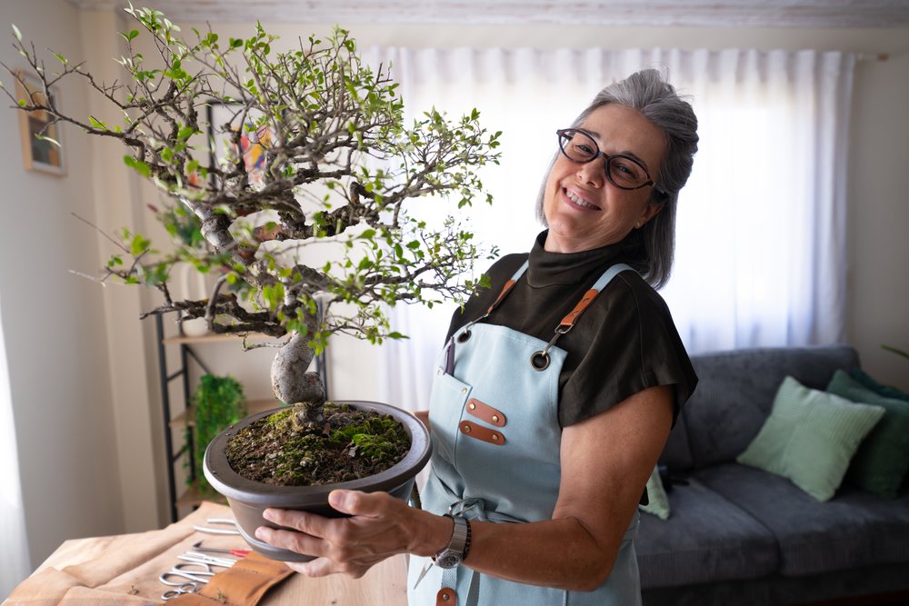 White woman holding a bonsai indoor plant in a living room