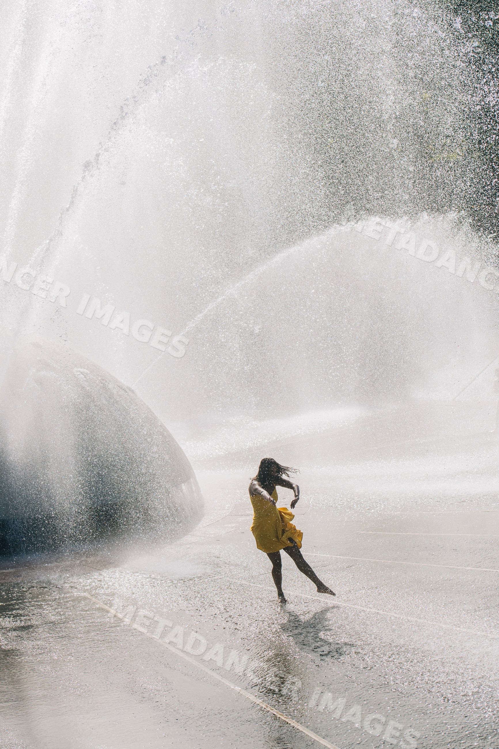 South Asian woman in yellow dress playing in water fountain outdoors