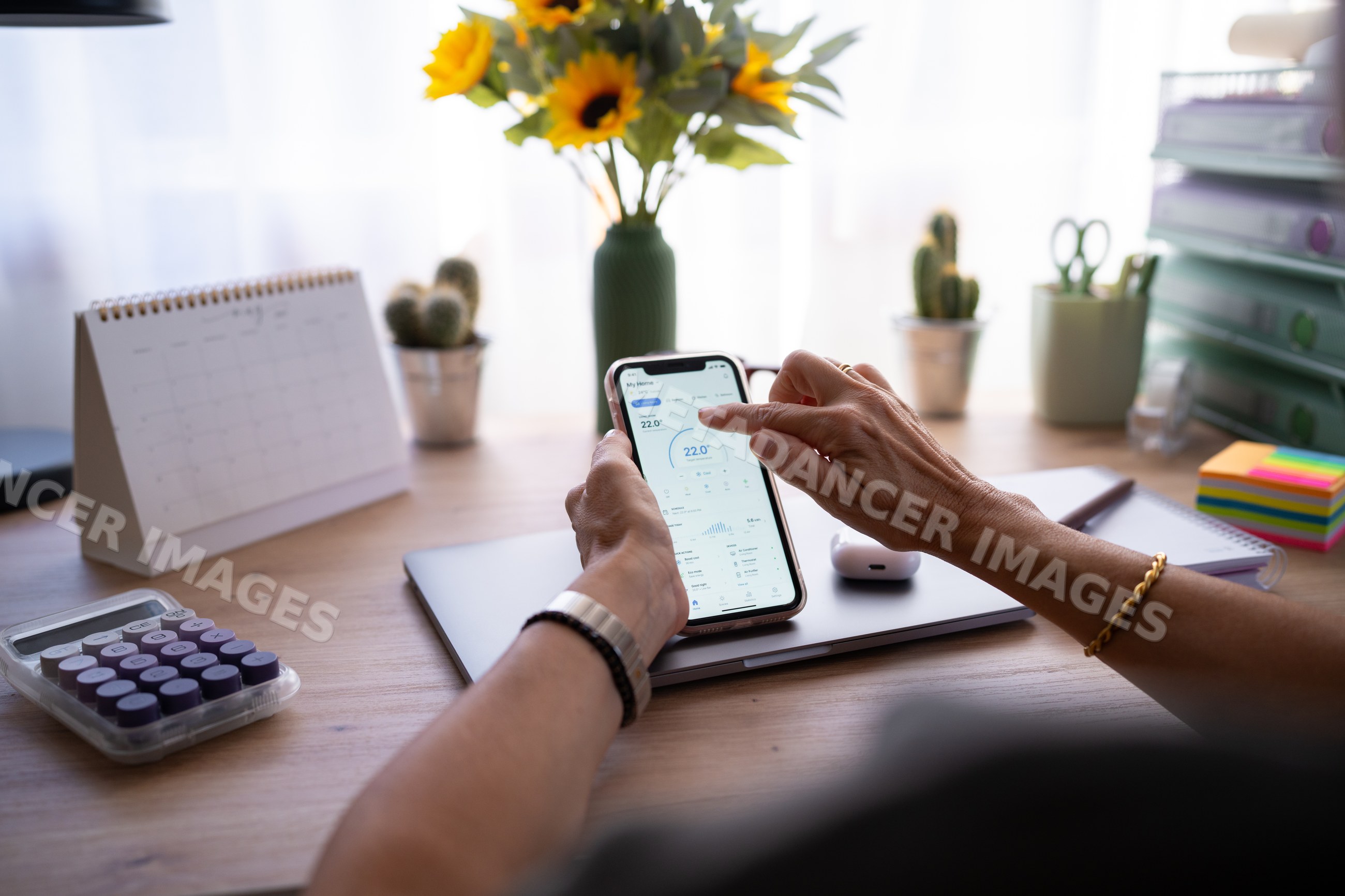 Hands using smartphone temperature control app on desk with office