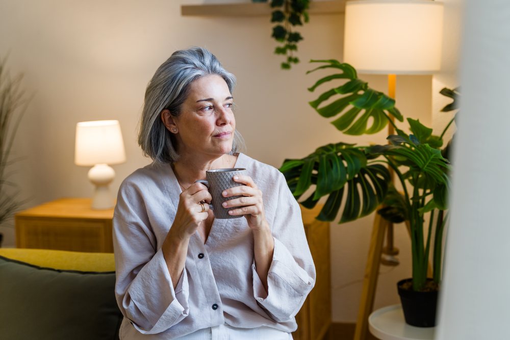 White woman relaxing indoors drinking coffee next to houseplant