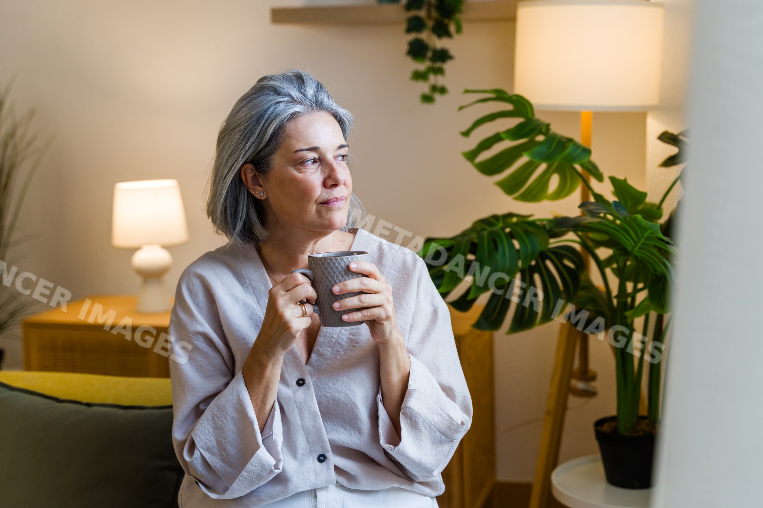 White woman relaxing indoors drinking coffee next to houseplant