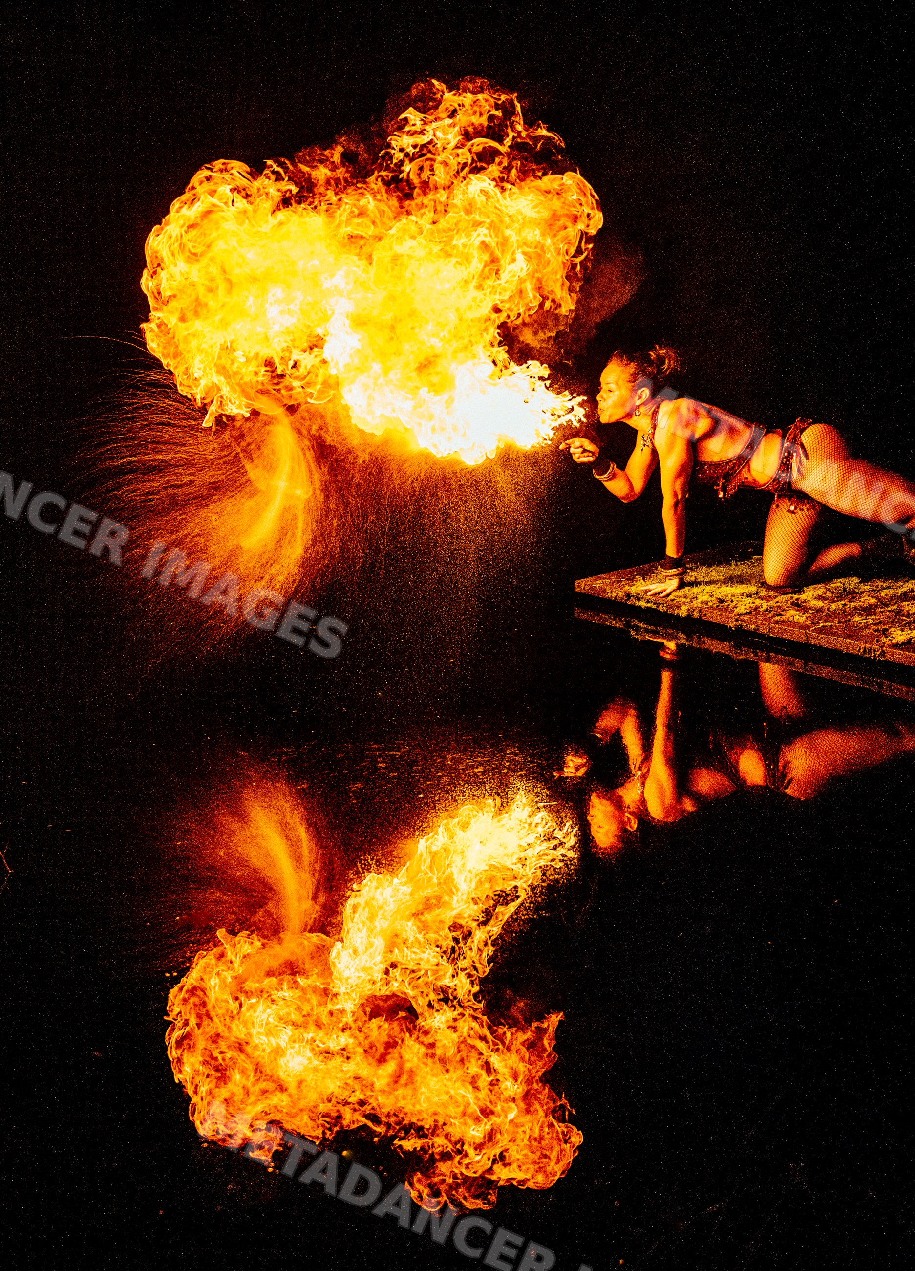 Fire breather performing at night with flames and reflection