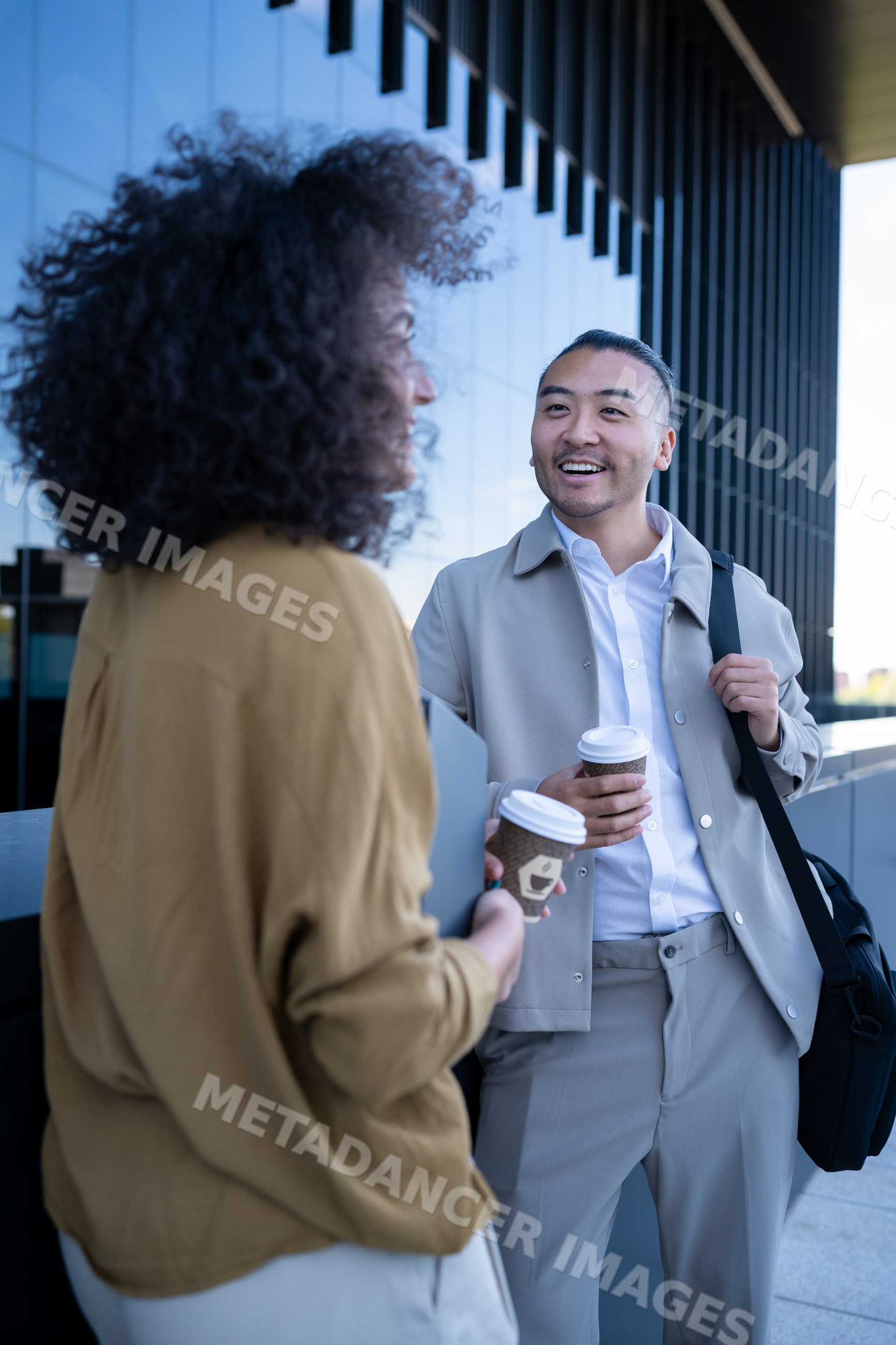 Two people holding coffee cups talking outside office building