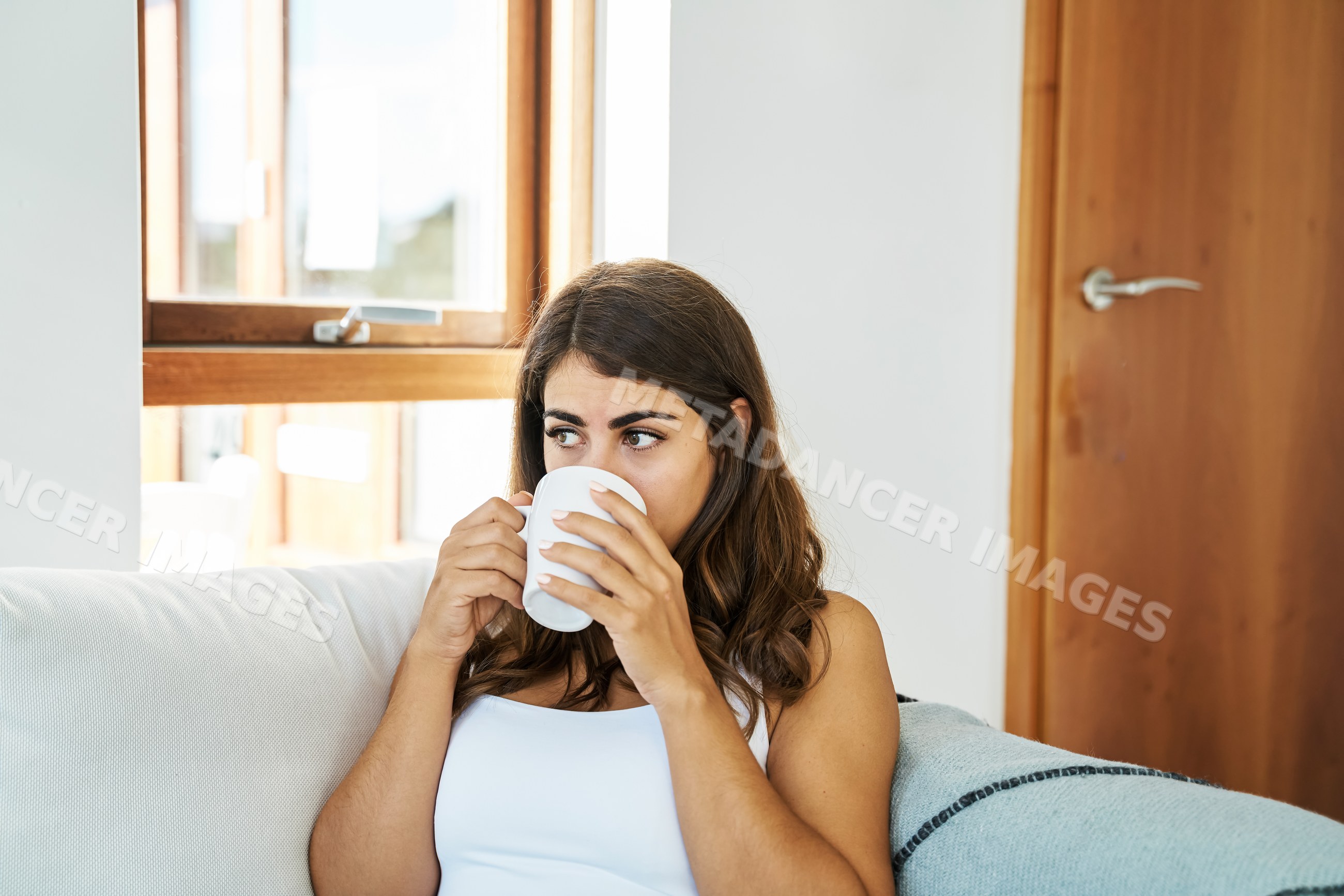 A young white woman drinks coffee on a couch inside a home in Iceland
