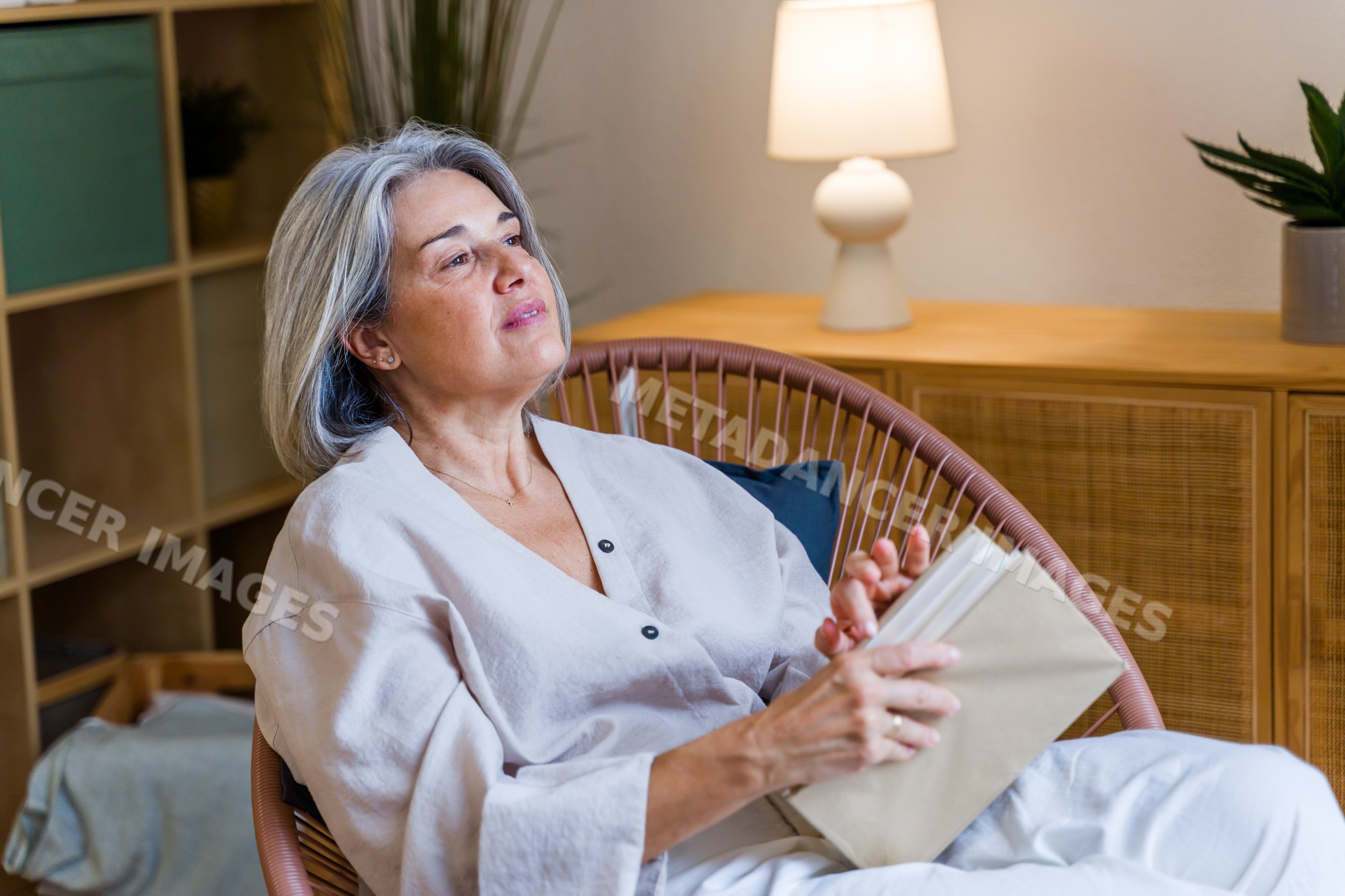 White woman reading book while relaxing in chair indoors