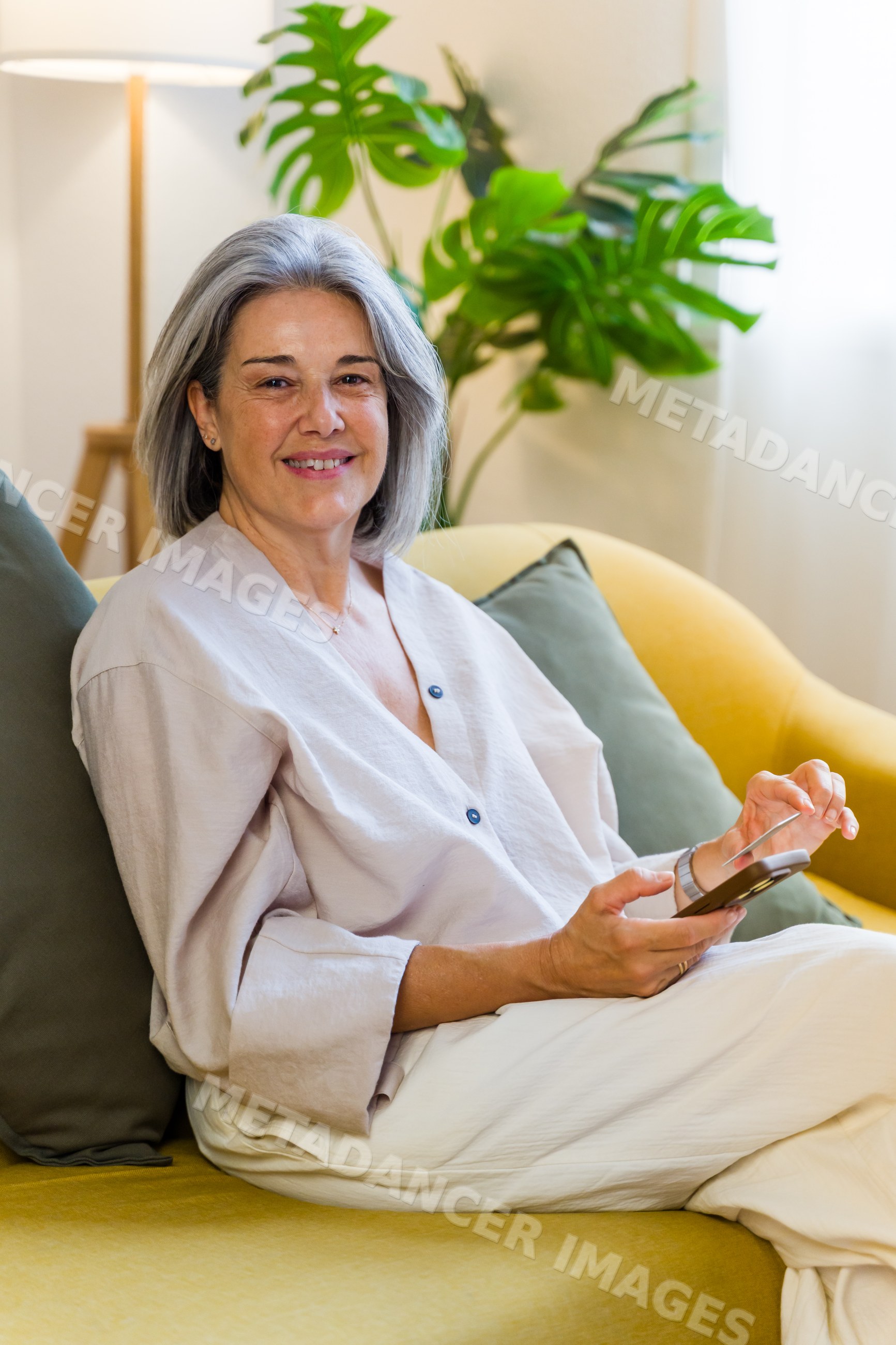 White woman sitting on yellow couch using tablet in living room