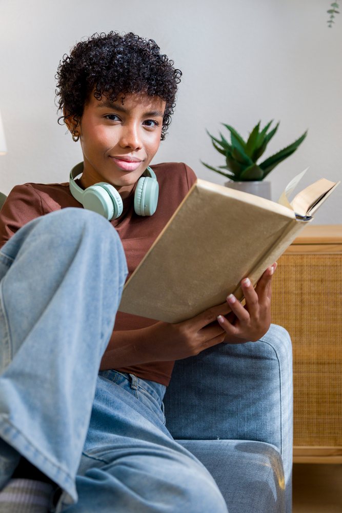Young African American woman reading with headphones at home on sofa
