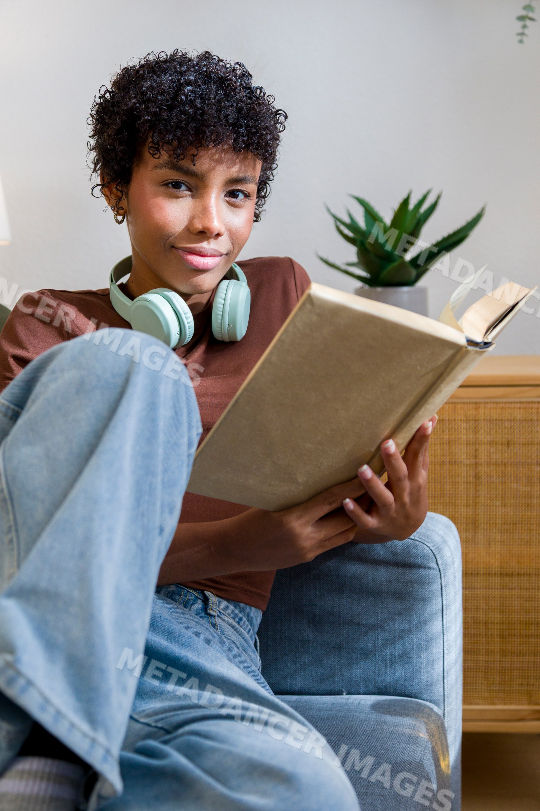 Young African American woman reading with headphones at home on sofa