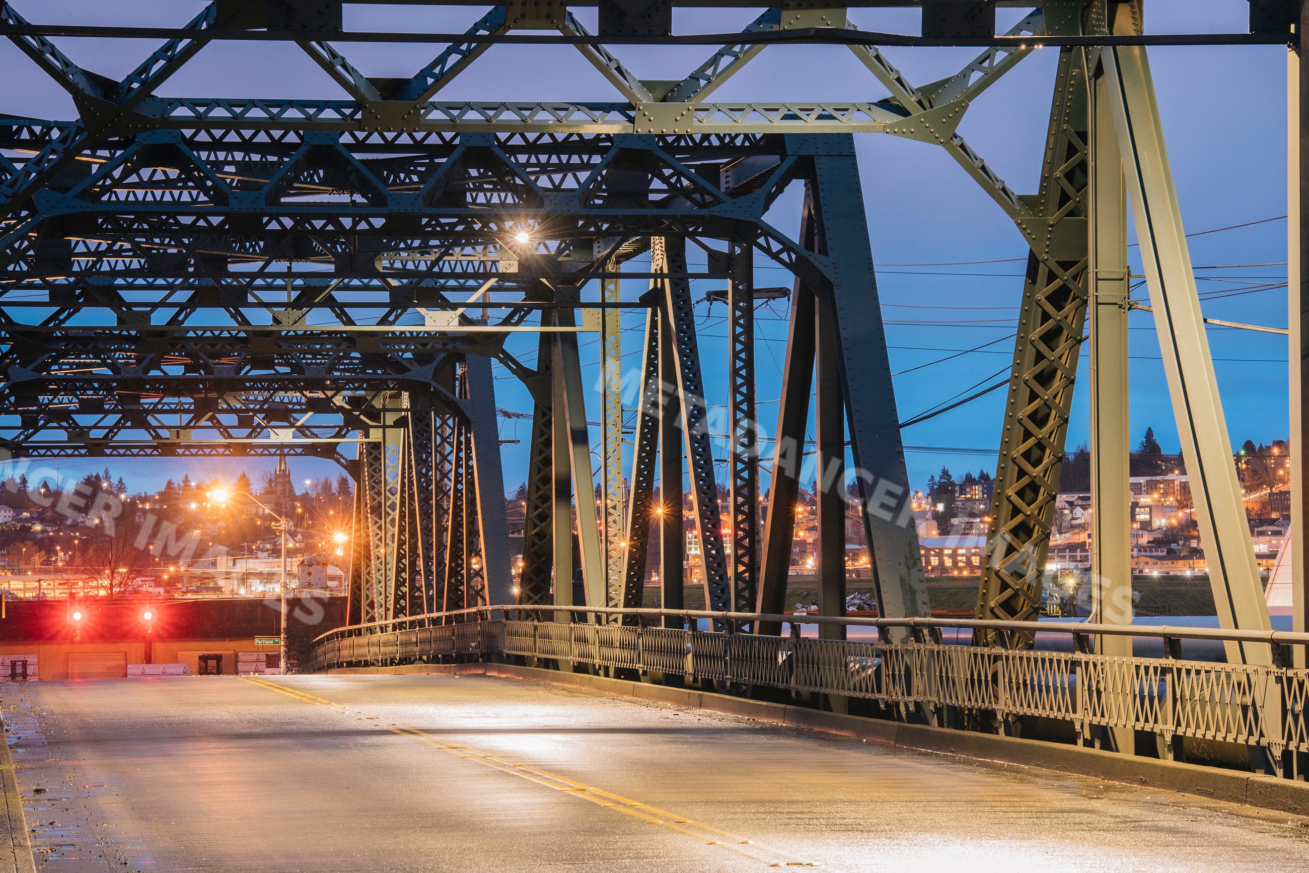 Metal truss bridge over roadway with cityscape at dusk in Tacoma