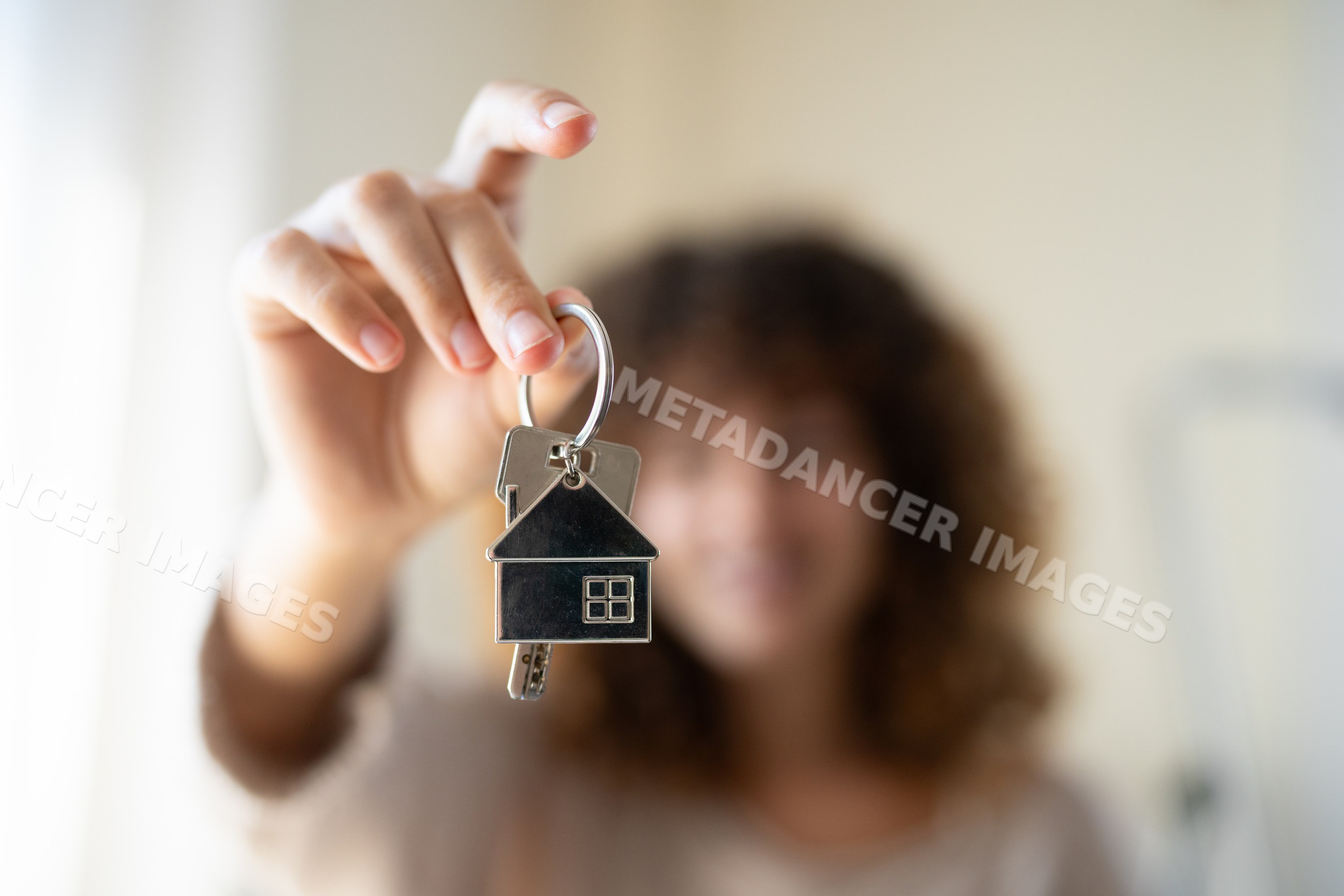 Keys with house-shaped keychain held indoors with blurred white person