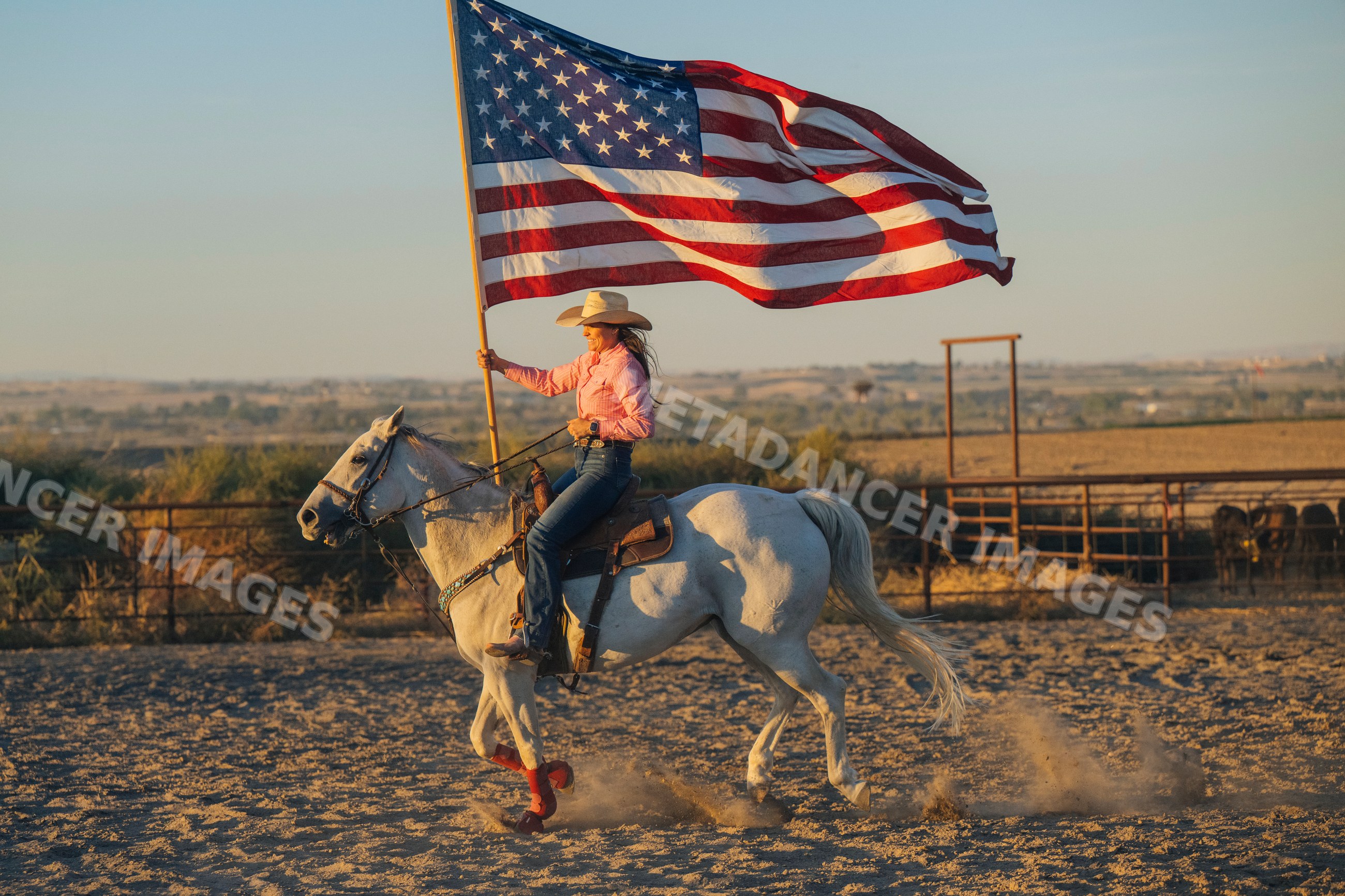 Cowgirl riding white horse carrying american flag