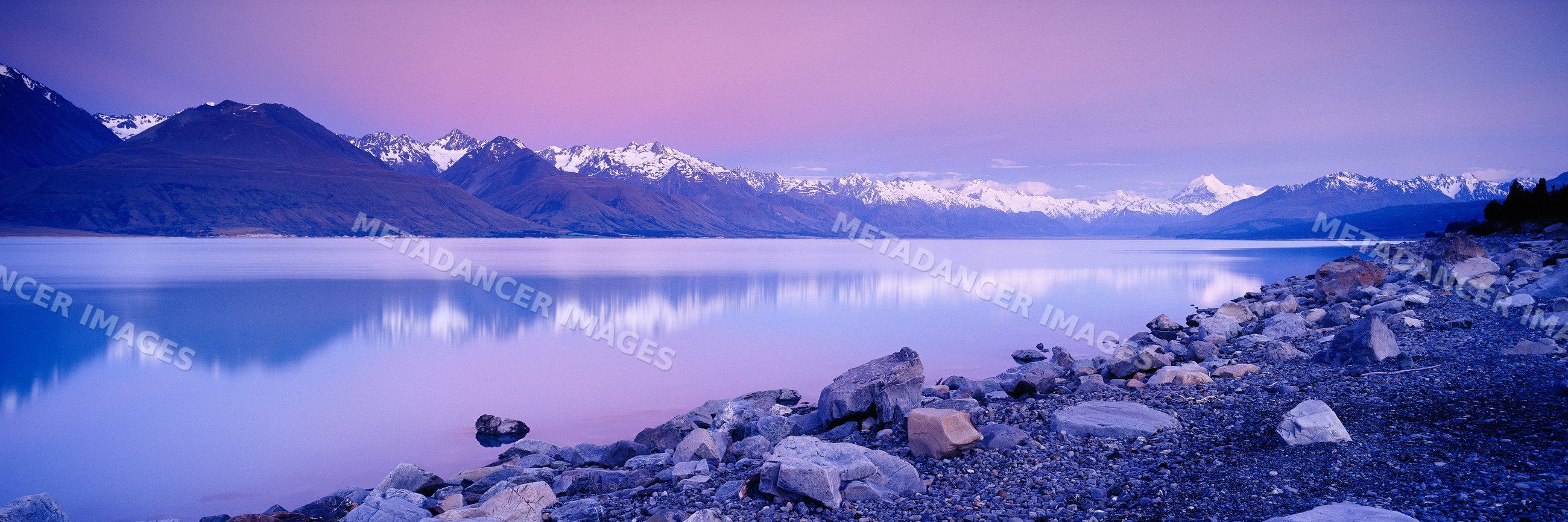 Mountains reflected in a calm lake at dusk with rocky shore