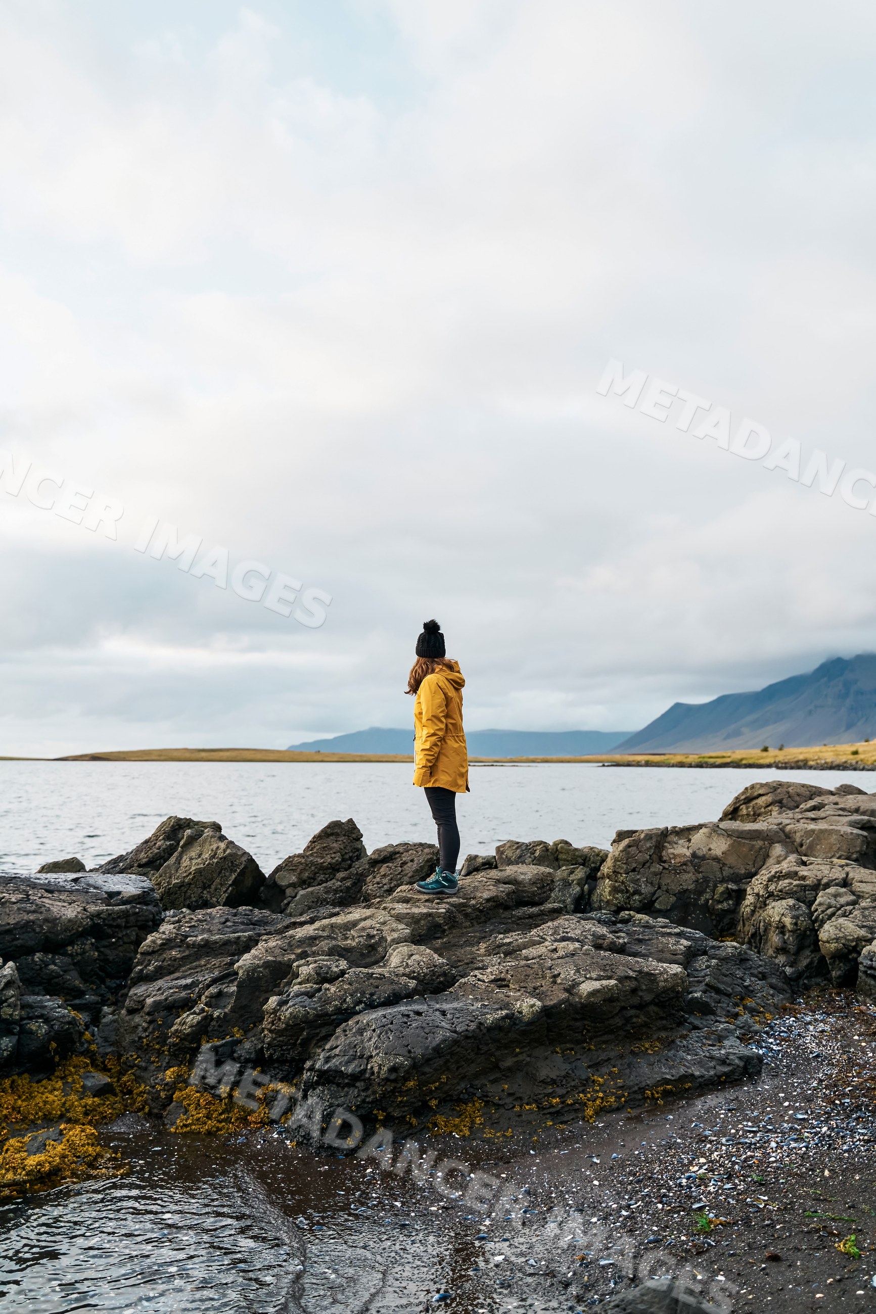 A white person stands on a rocky shoreline overlooking water