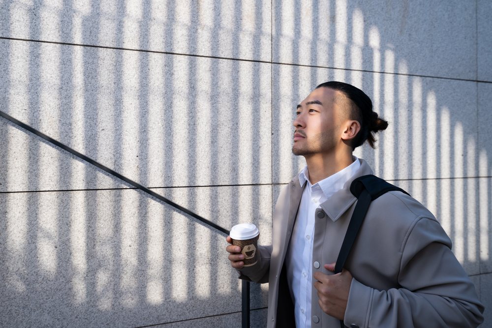Man holding coffee cup with vertical shadows on concrete wall
