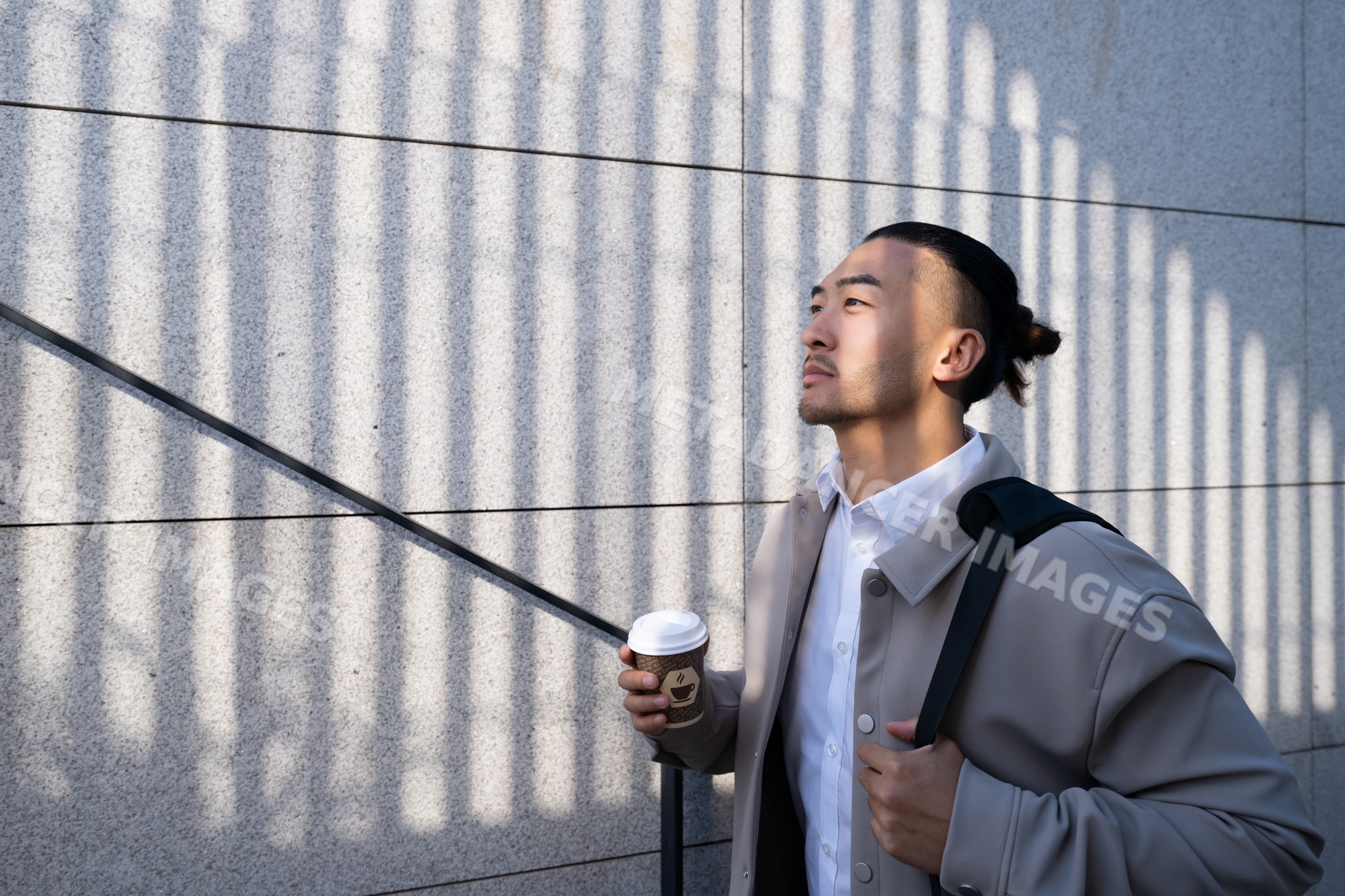 Man holding coffee cup with vertical shadows on concrete wall