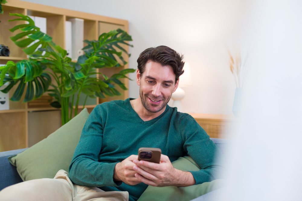 White man sitting on couch using smartphone in cozy living room