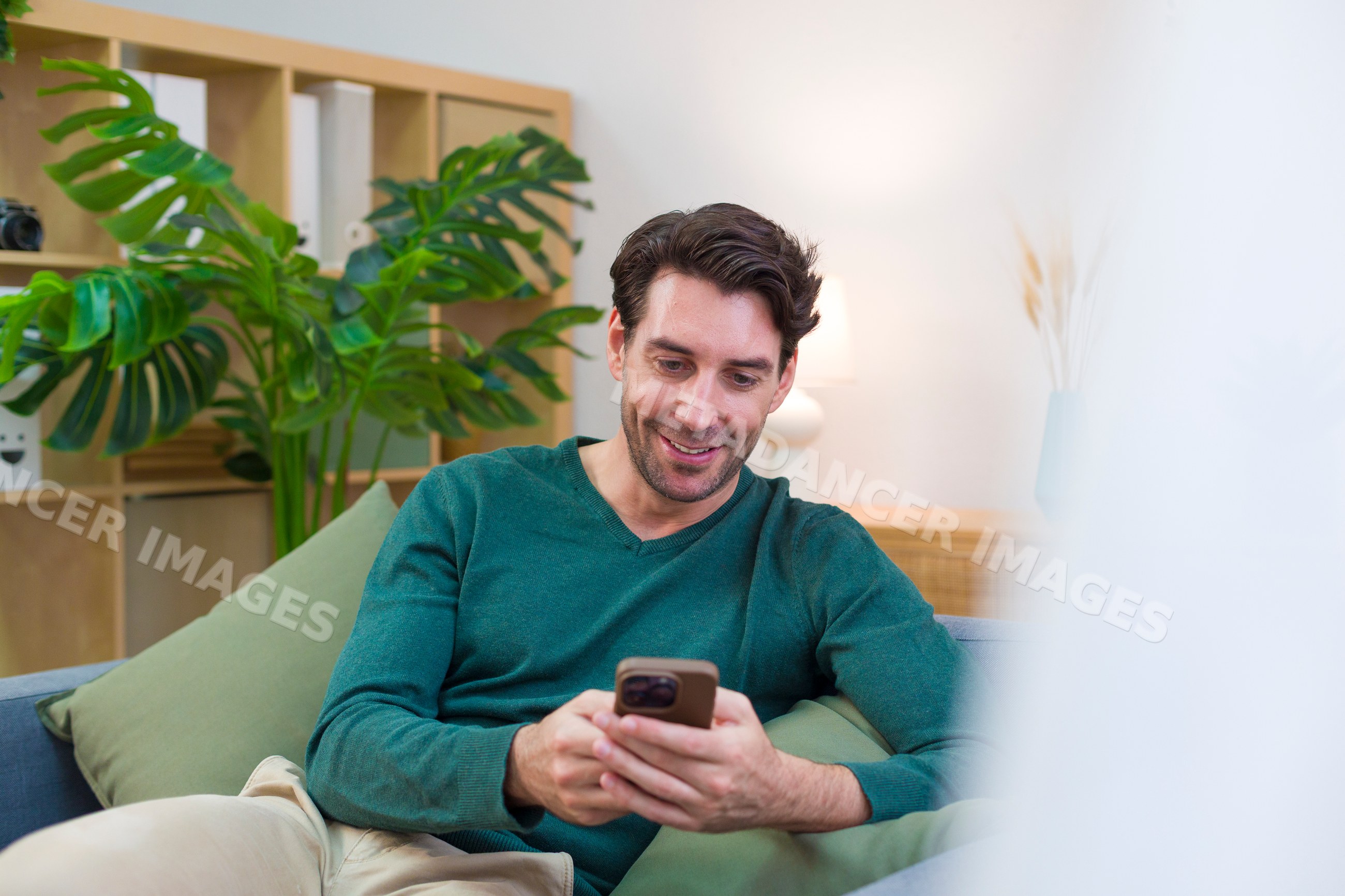 White man sitting on couch using smartphone in cozy living room