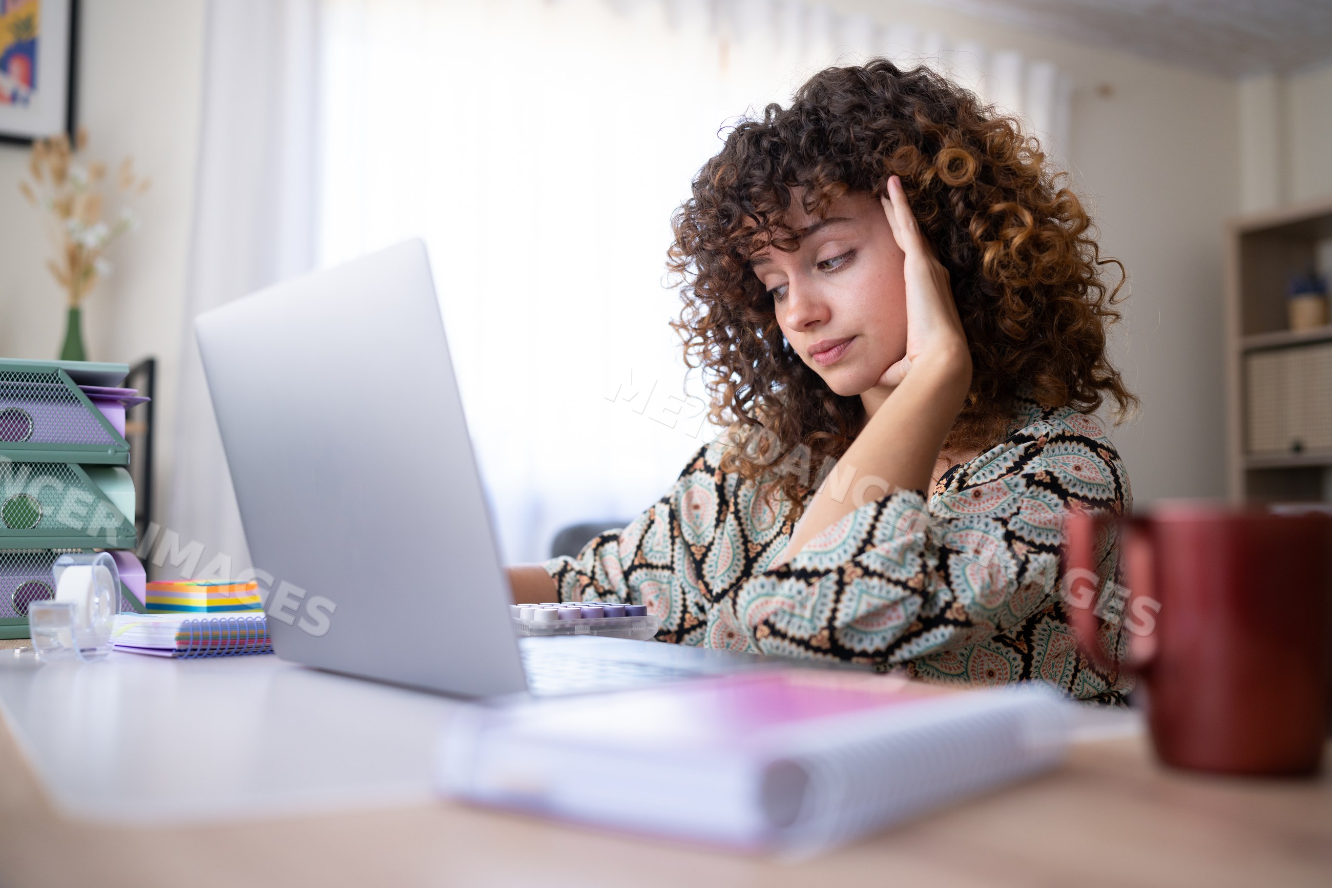White woman with curly hair working on laptop at home office desk