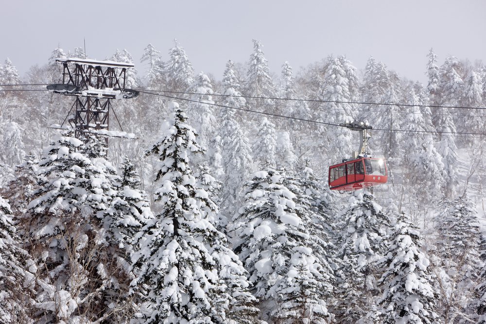 Red cable car ski lift over snowy forest japan