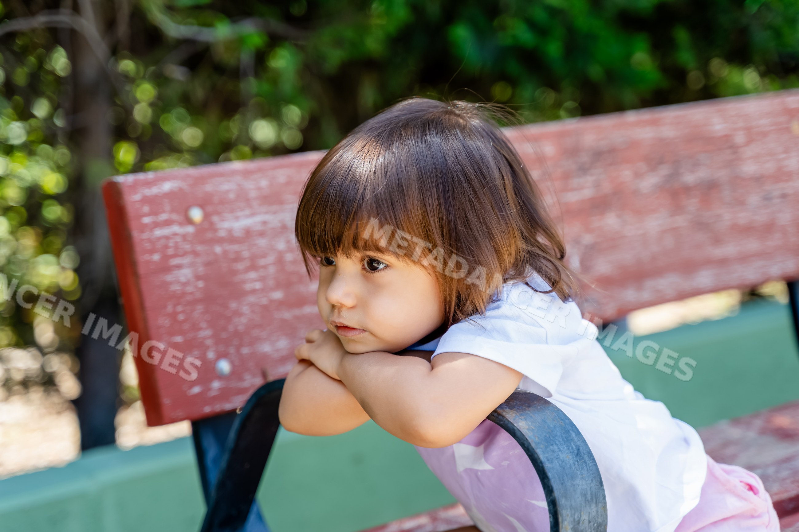White child leaning on wooden bench armrest outdoors on a summer day