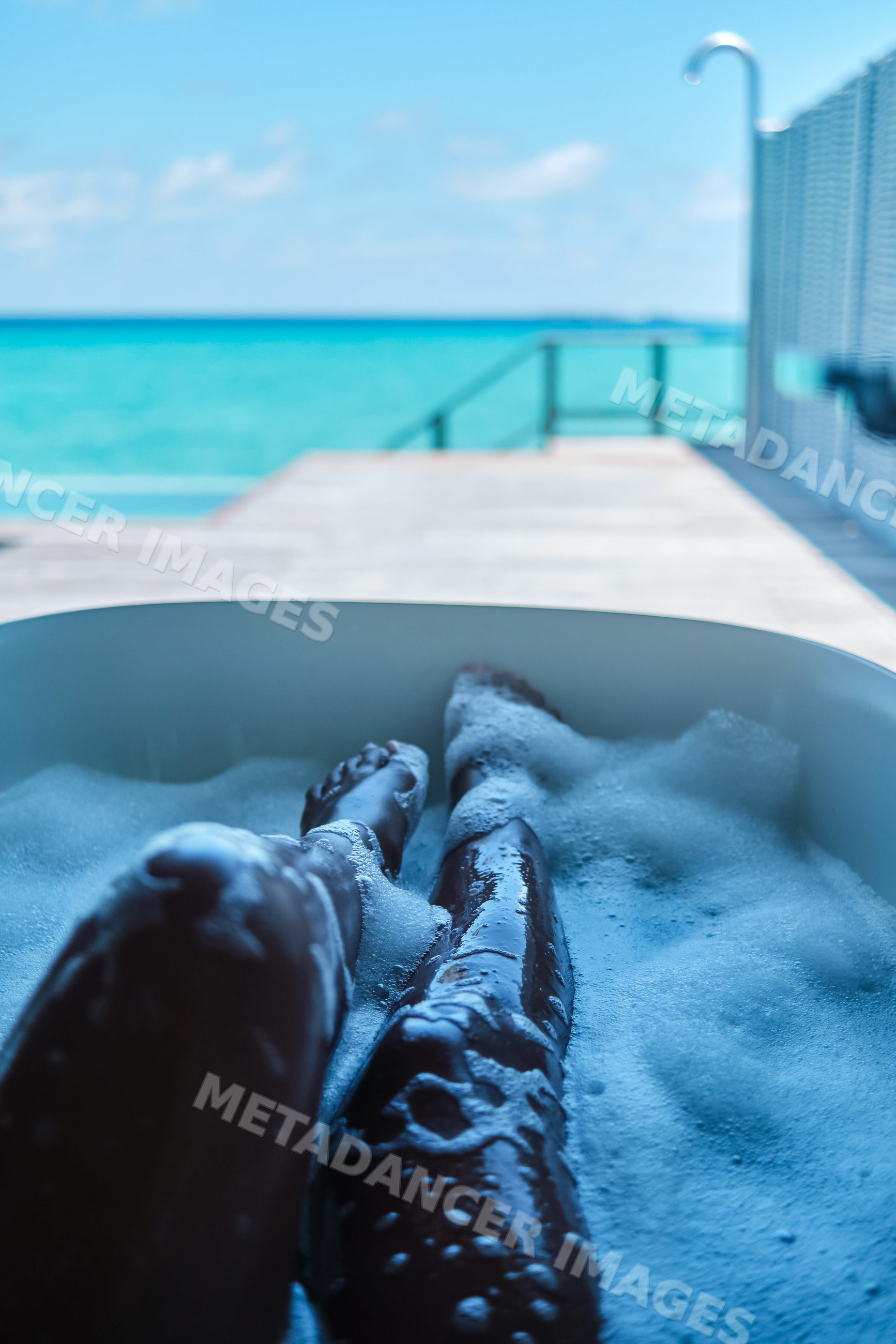 A white person soaks legs in bubble bath with ocean view