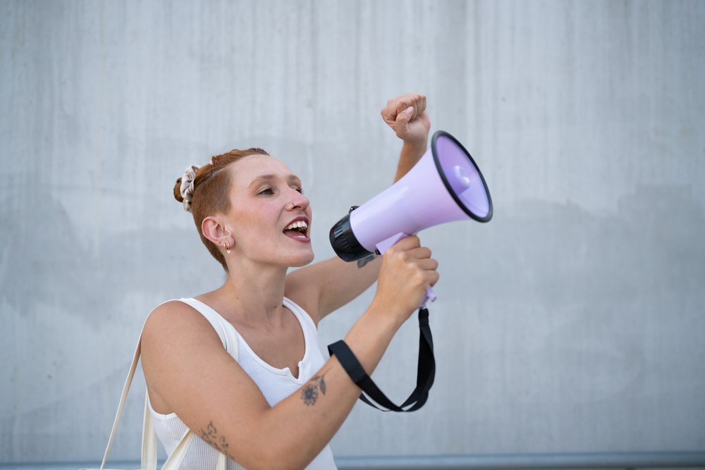 A white woman speaks passionately into a megaphone in an urban setting