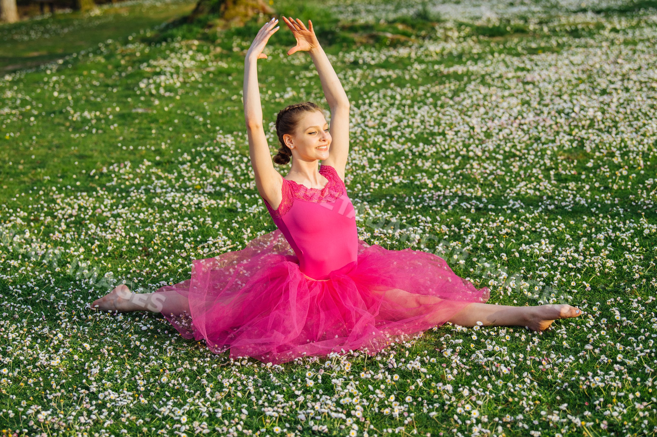 Ballerina in pink tutu performing split in daisy-covered field