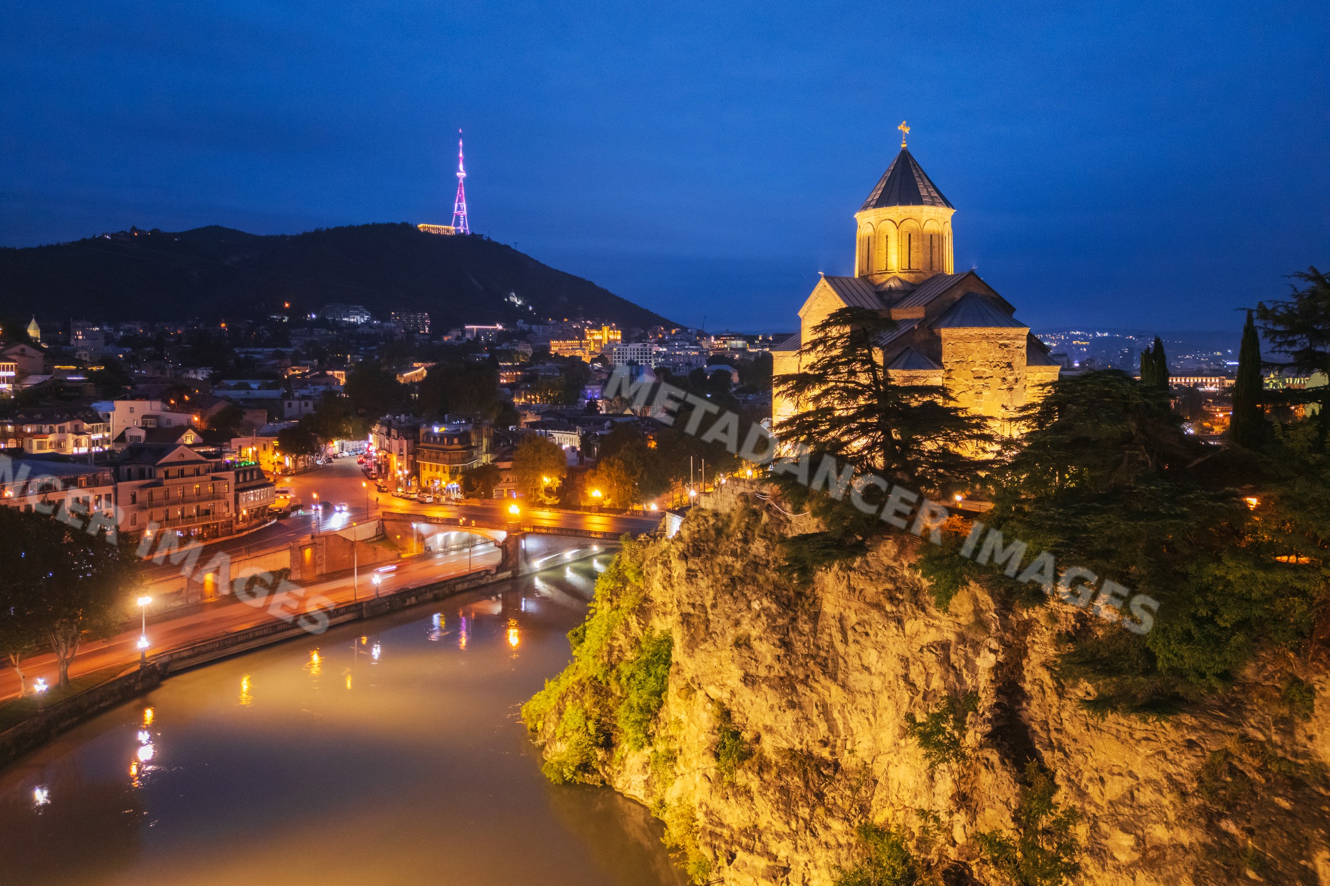 Metekhi Church illuminated above mtkwari river in tbilisi at night