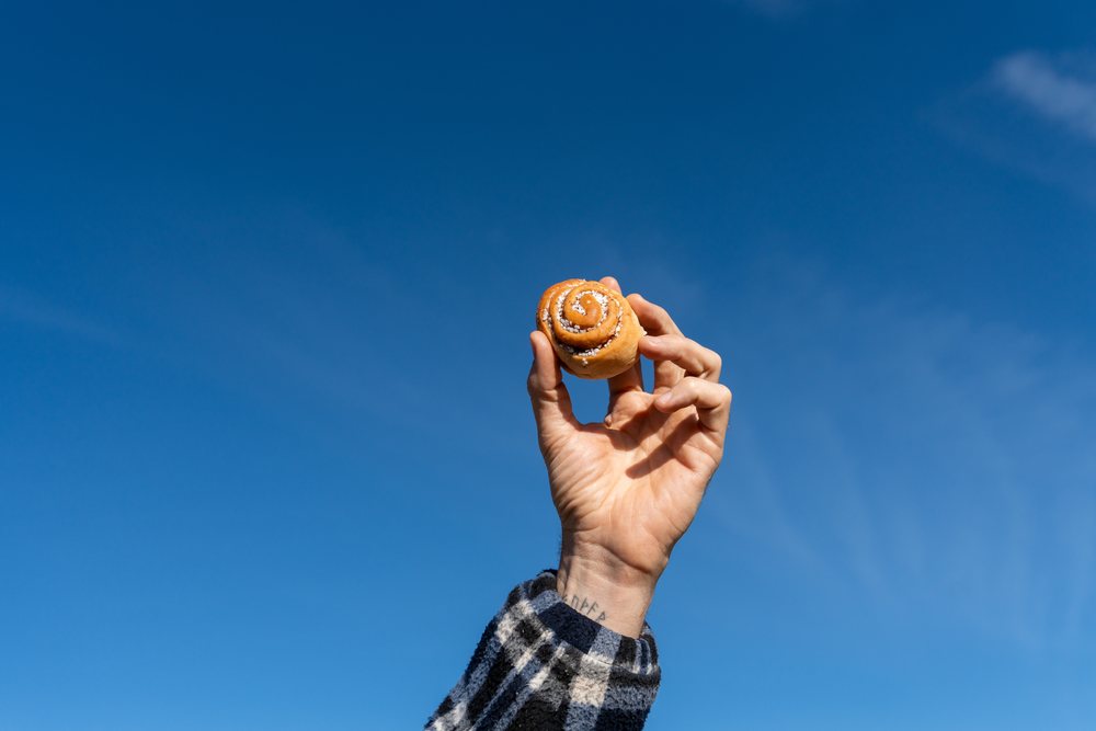 Hand holding cinnamon roll pastry against blue sky outdoors Norway