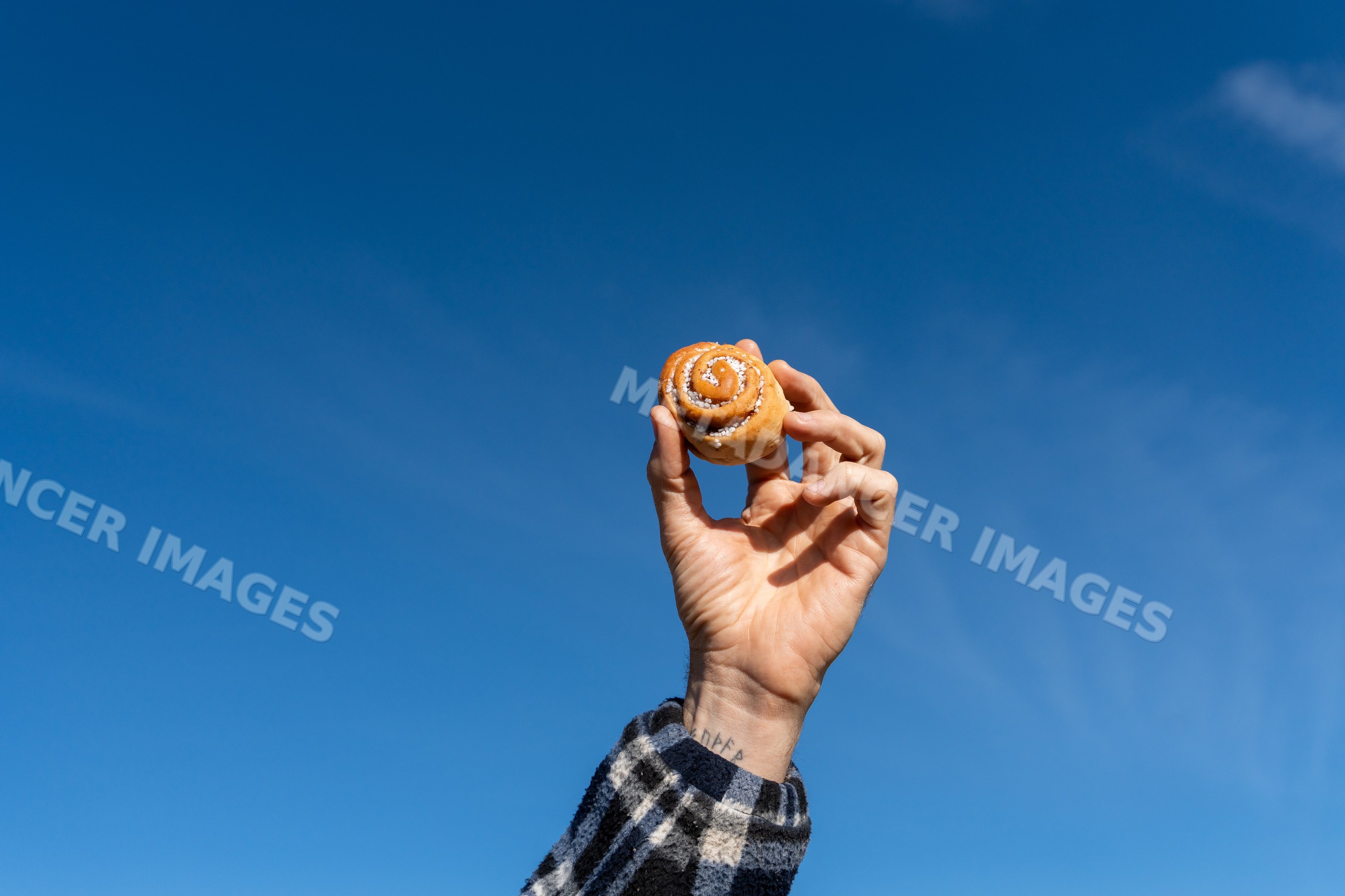 Hand holding cinnamon roll pastry against blue sky outdoors Norway