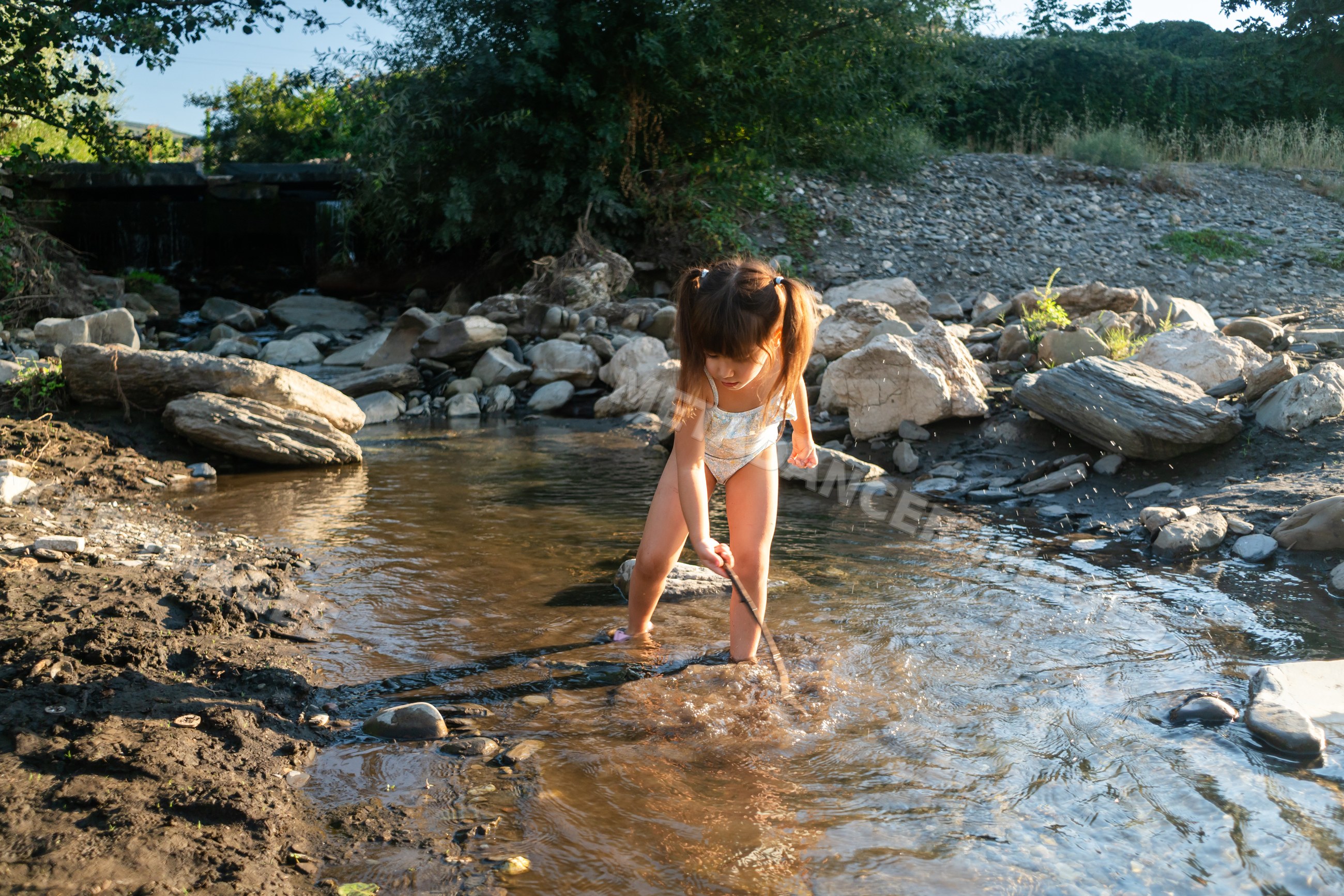 A young white child playing with a stick in a shallow creek outdoors