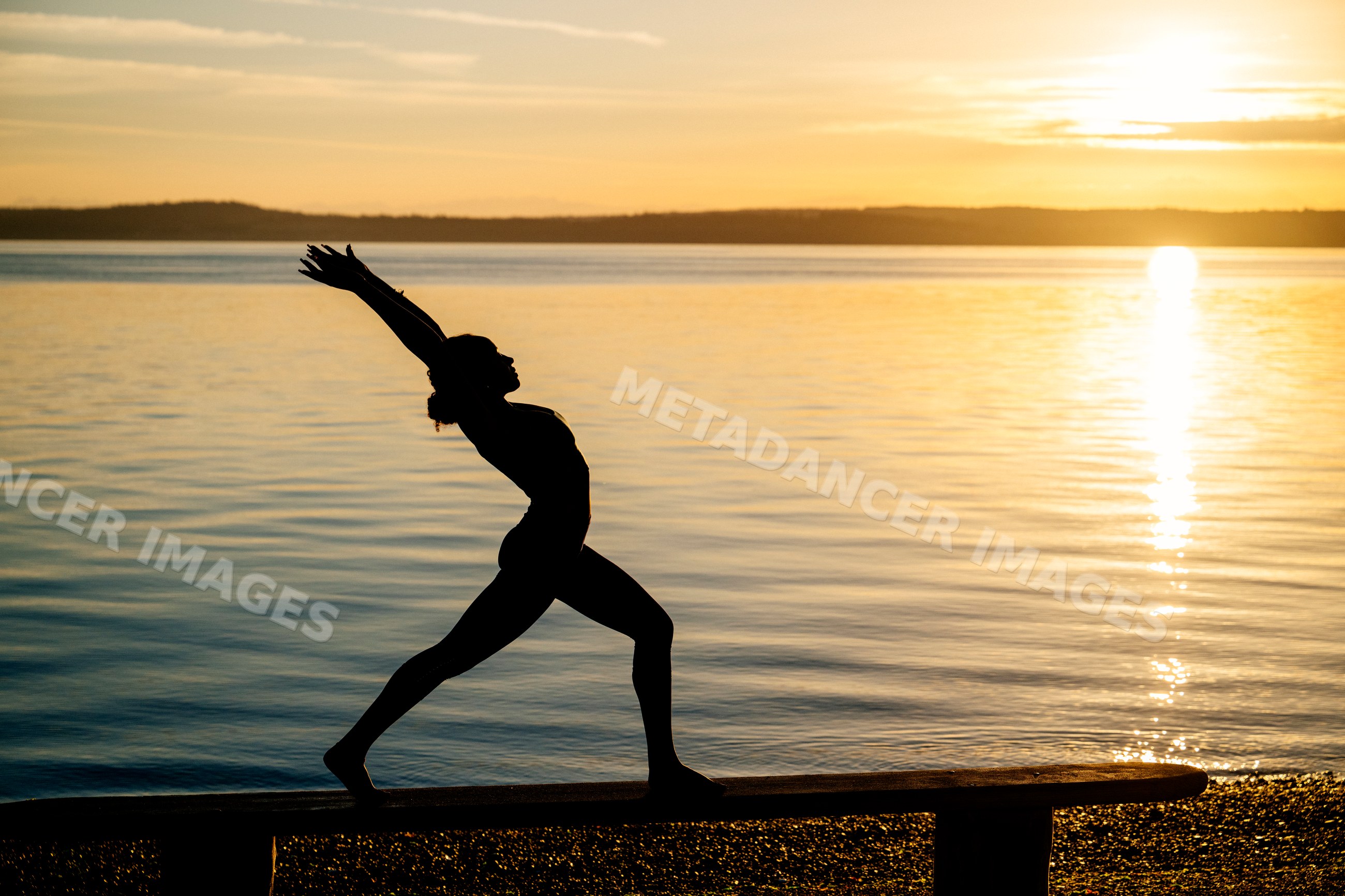 Hispanic woman performing yoga stretch pose by lake at sunset in USA