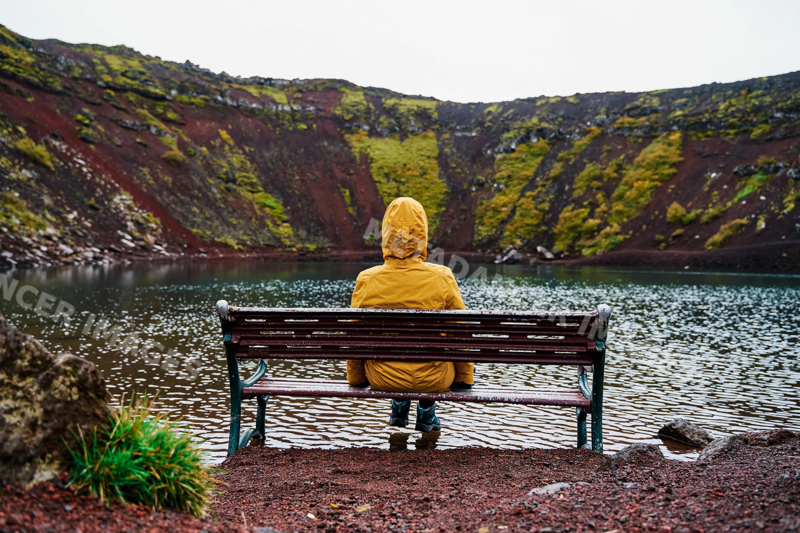 A white person sits on a bench reflecting by a volcanic crater lake