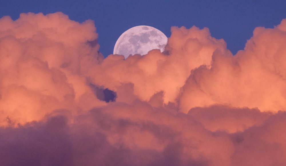 Full moon rising among colorful sunset clouds in twilight sky