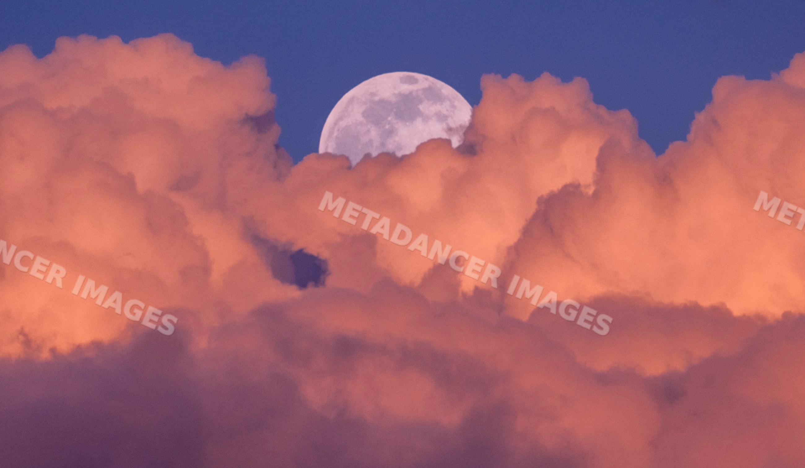 Full moon rising among colorful sunset clouds in twilight sky
