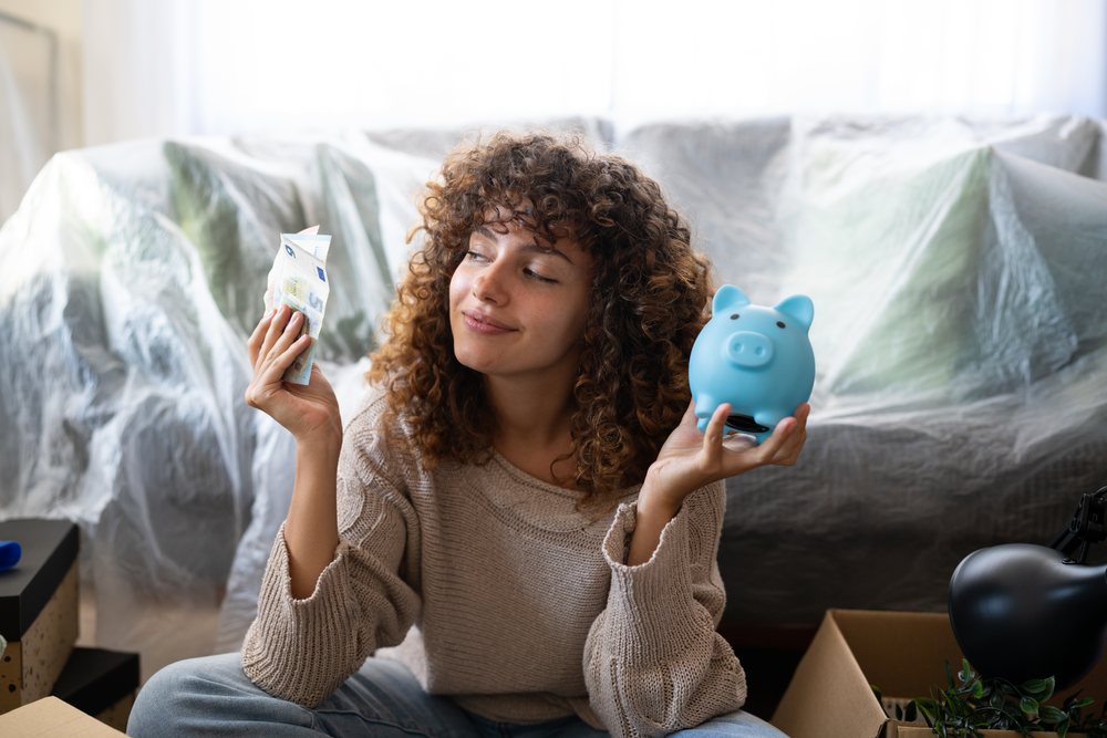 White woman holding euro cash and blue piggy bank indoors