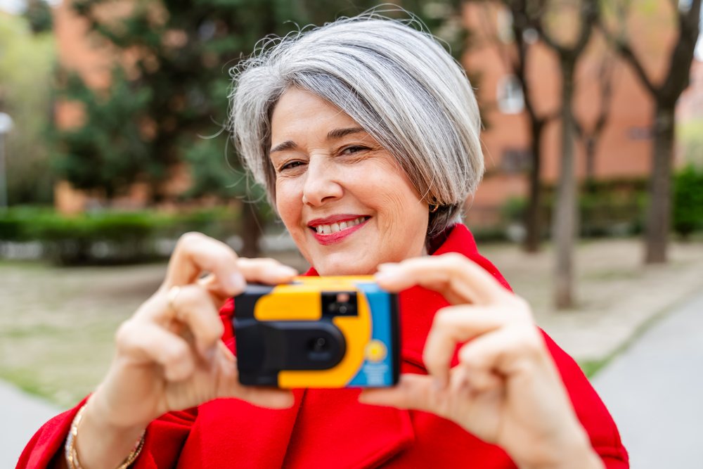 White woman smiling and taking photo with disposable camera outdoors