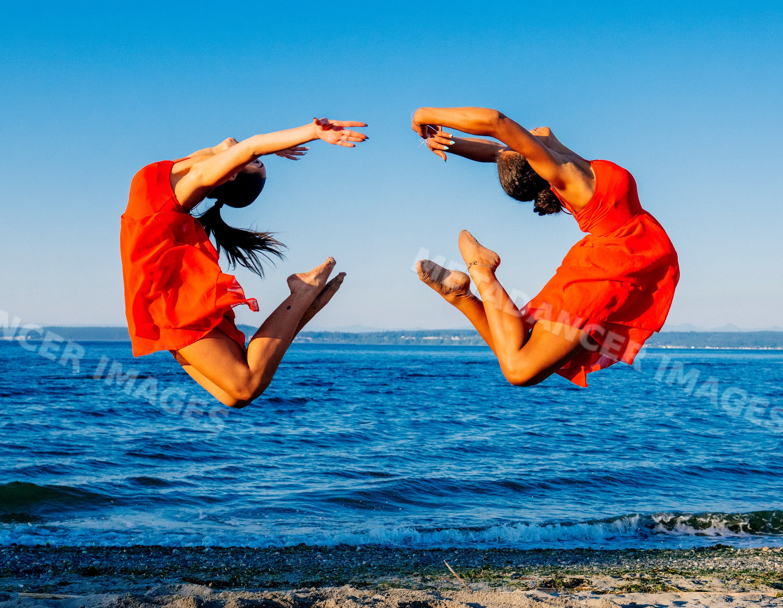 Two women in red dresses perform synchronized jumps at the beach