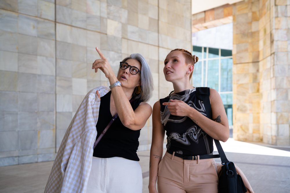 Two white women pointing and talking outside modern stone building