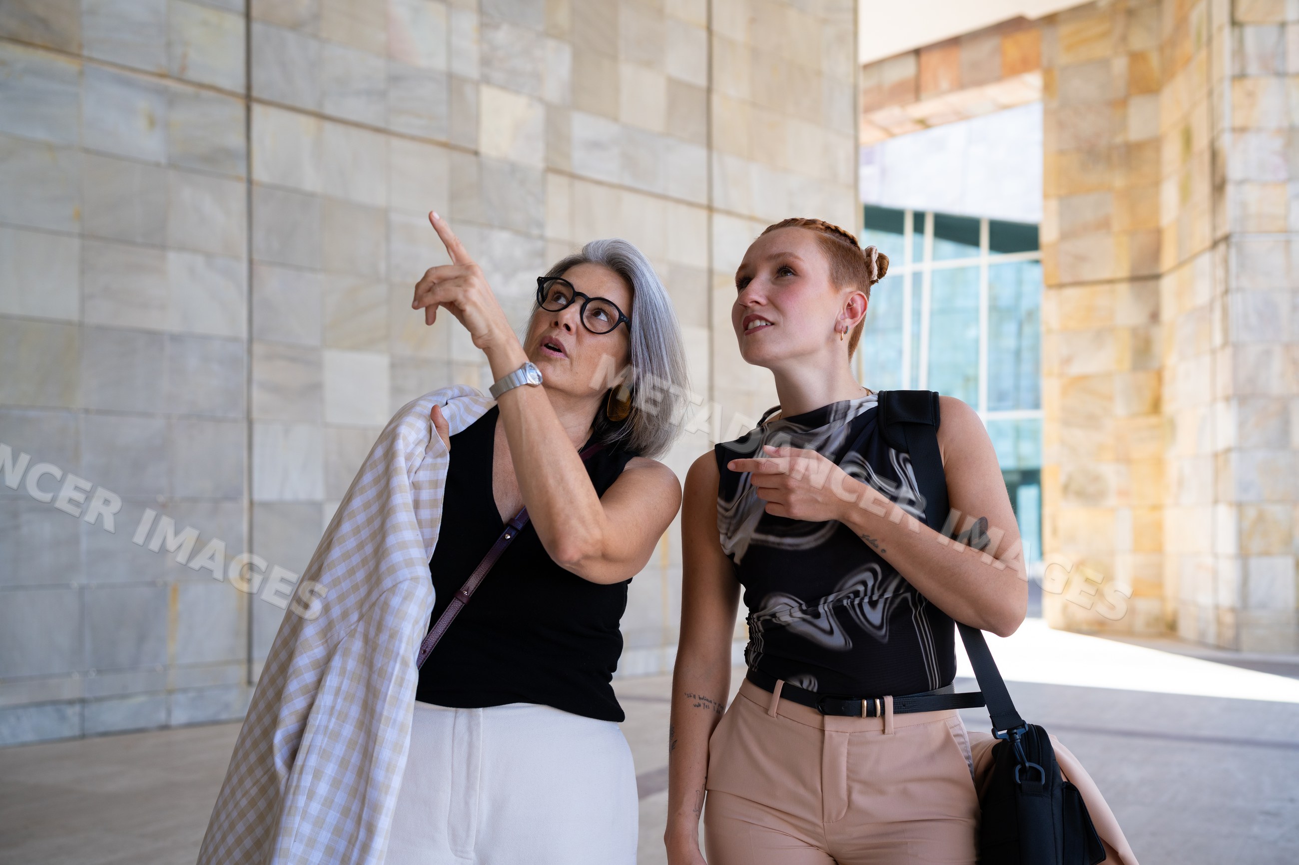 Two white women pointing and talking outside modern stone building