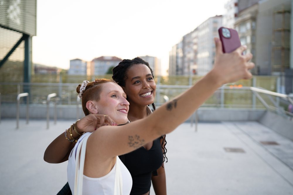 Two white and African American women taking a selfie outdoors